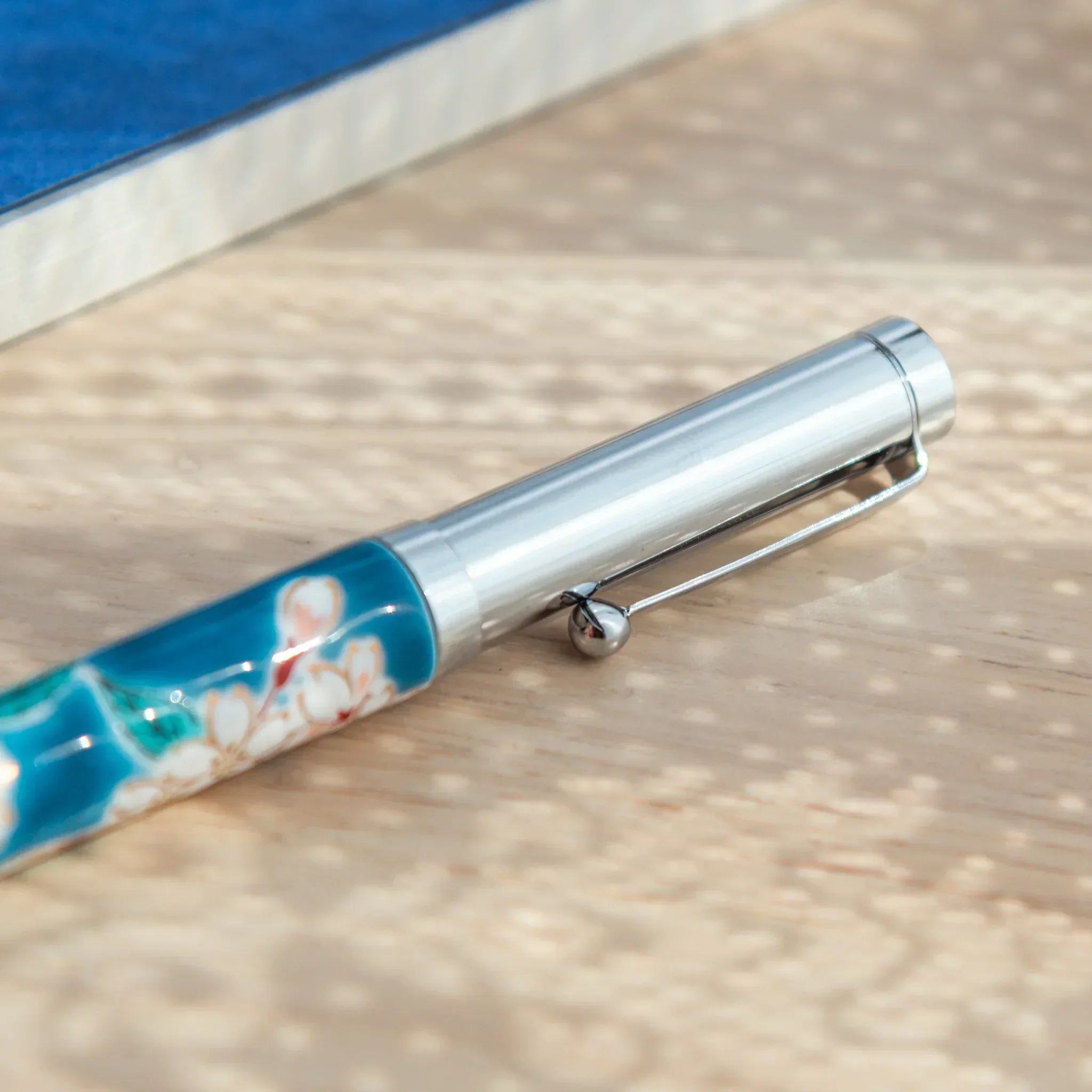 Detail of the silver cap of a Sakura Kutani Japanese Ballpoint Pen with blossom motif visible below.