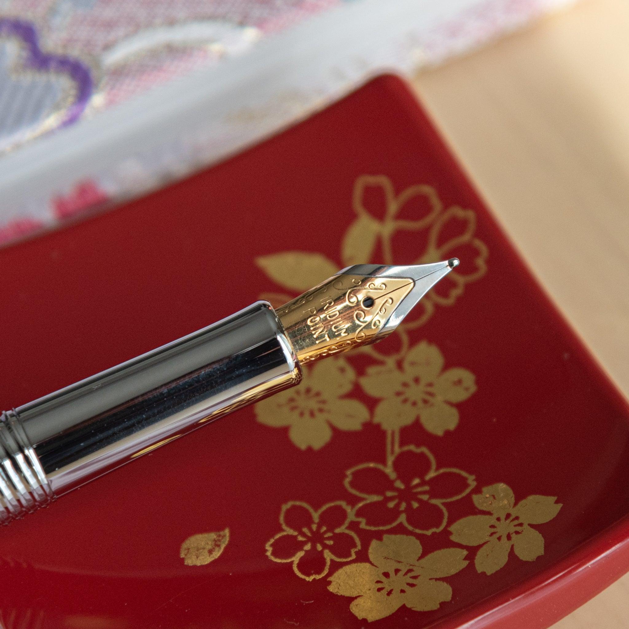 A close-up of a fountain pen’s gold nib placed on a red dish with floral patterns.