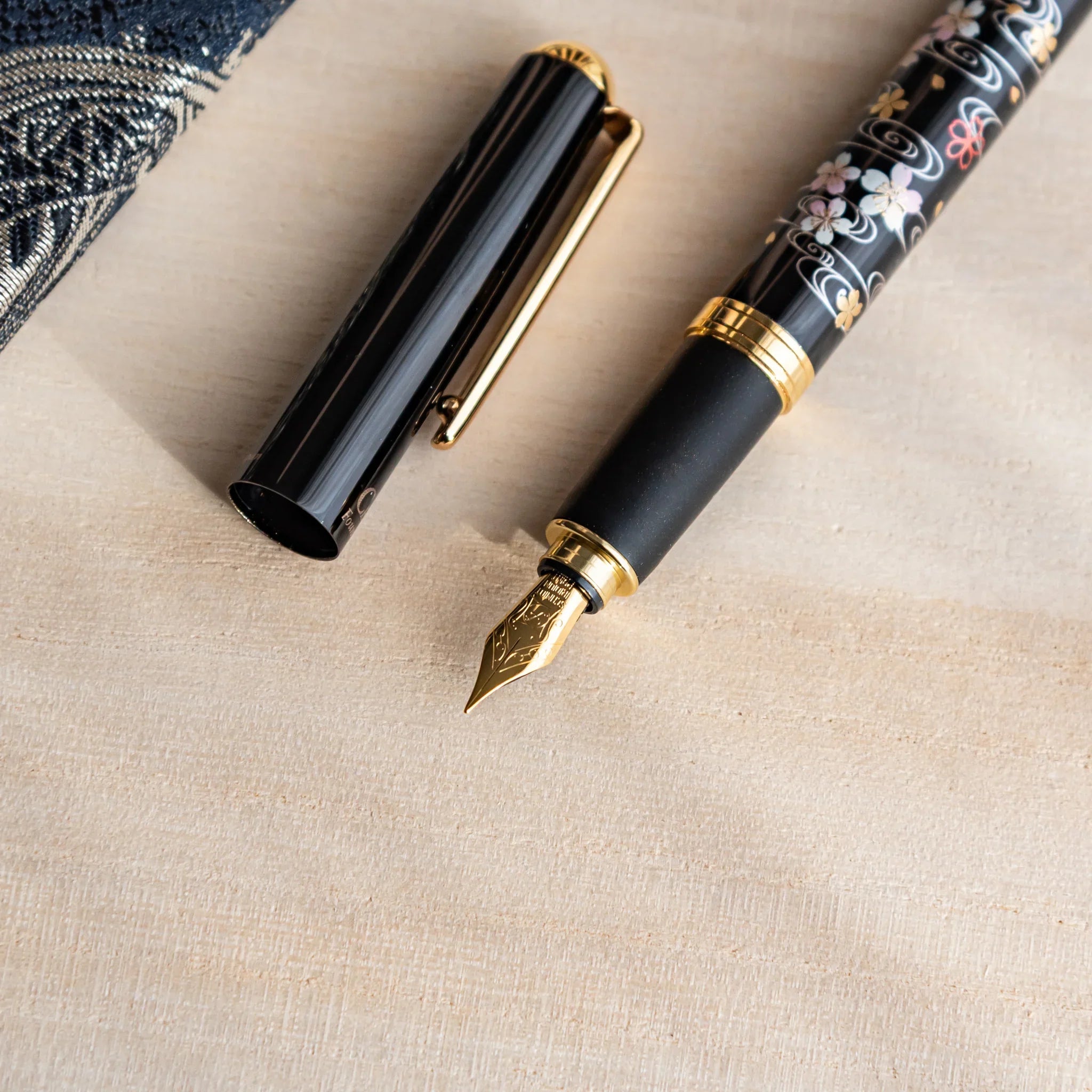 Uncapped black Yamanaka fountain pen with gold nib and sakura river motifs, placed on a desk.