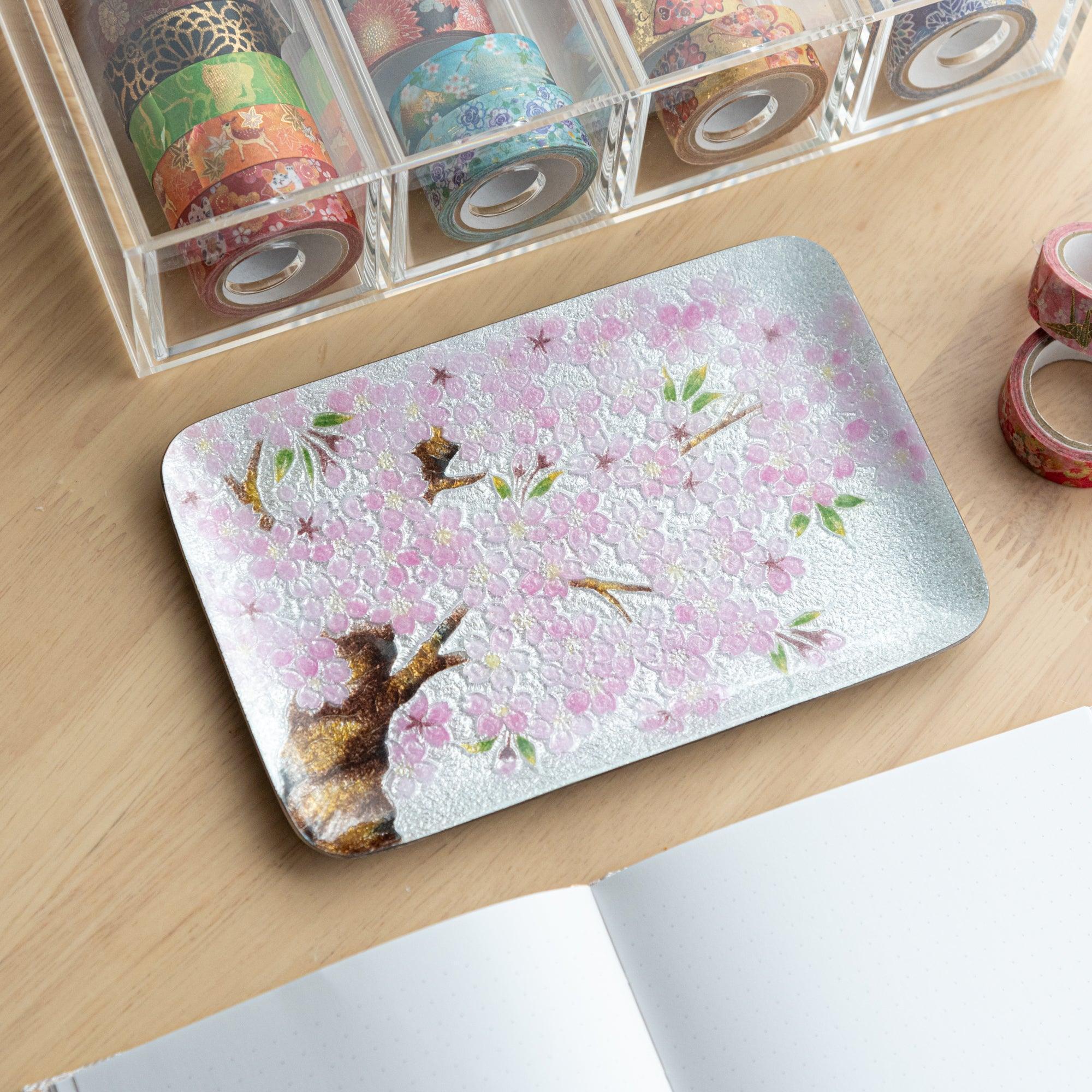 Silver tray with pink cherry blossoms and brown branches, showcasing a delicate floral design on a textured surface.