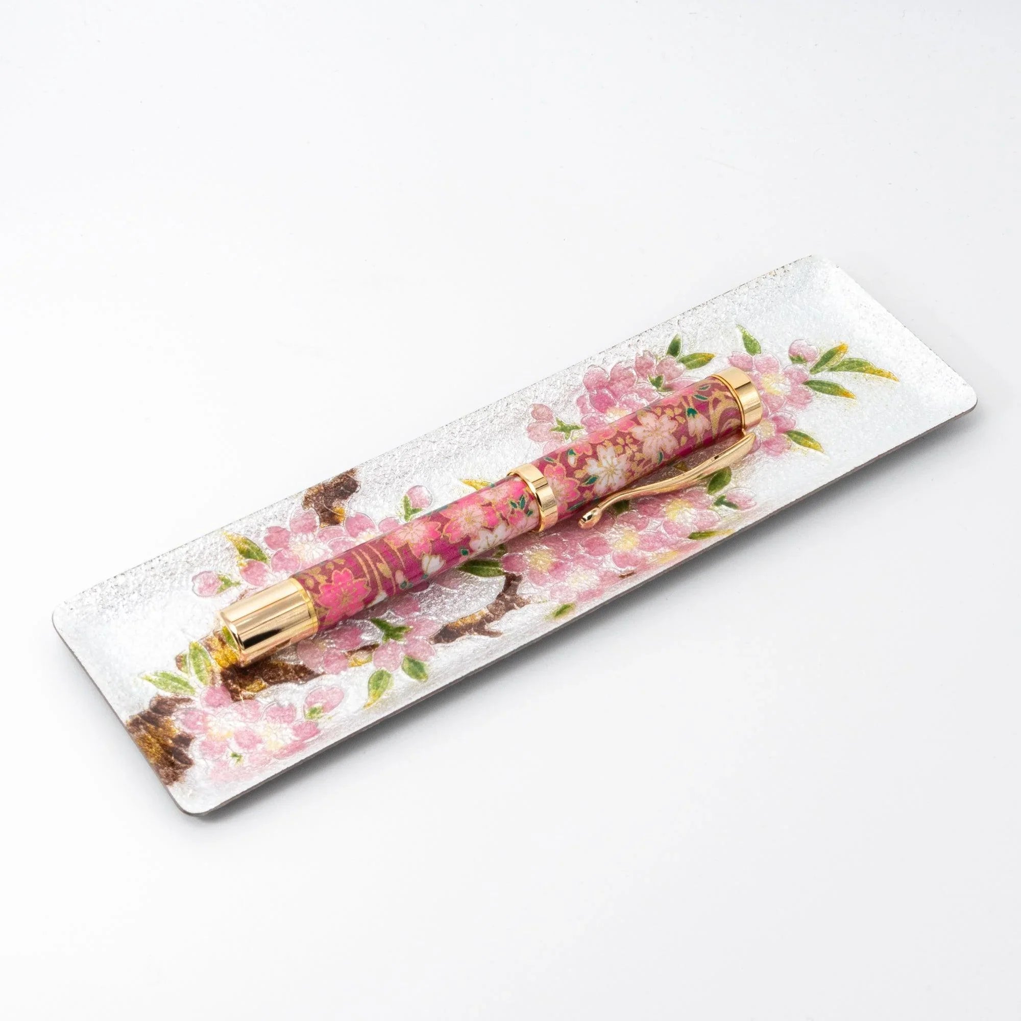 Silver enamel slim pen tray with sakura design on white background, angled view, pink sakura print pen resting on tray