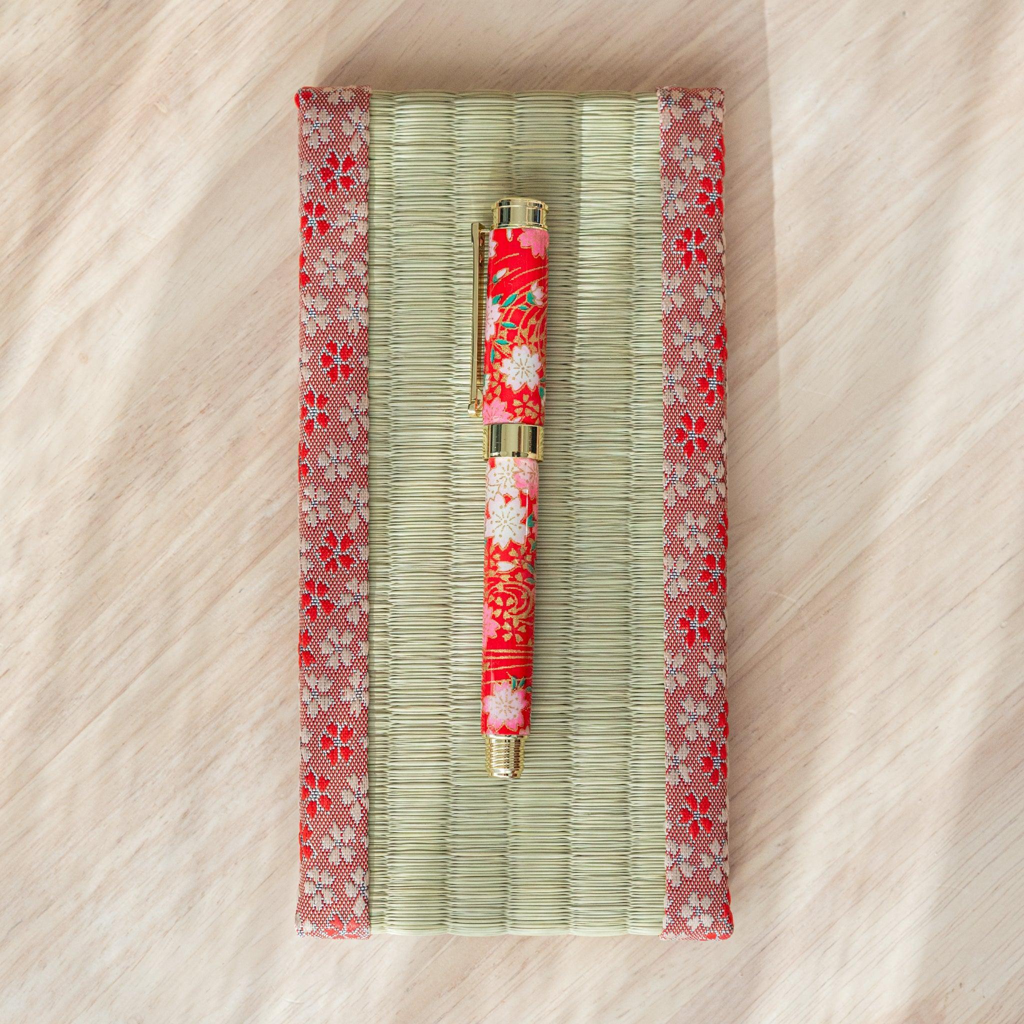 A red floral Japanese stationery fountain pen on a tatami-style mat under soft lighting.