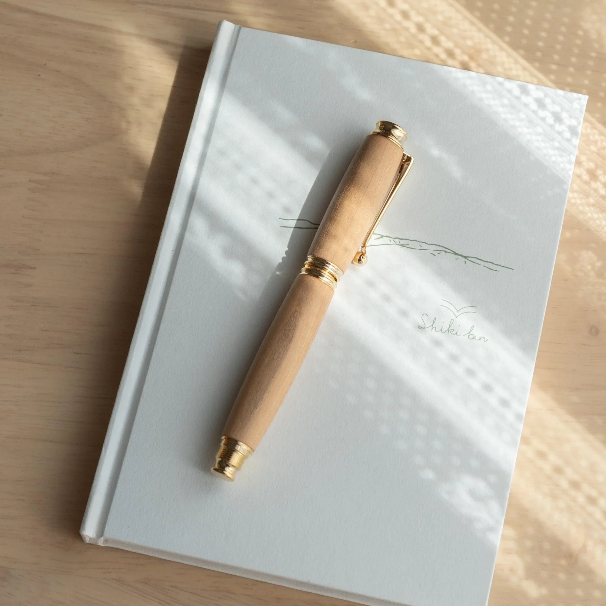 Natural wood Japanese fountain pen body uncapped on a white notebook in natural sunlight, angled view from above