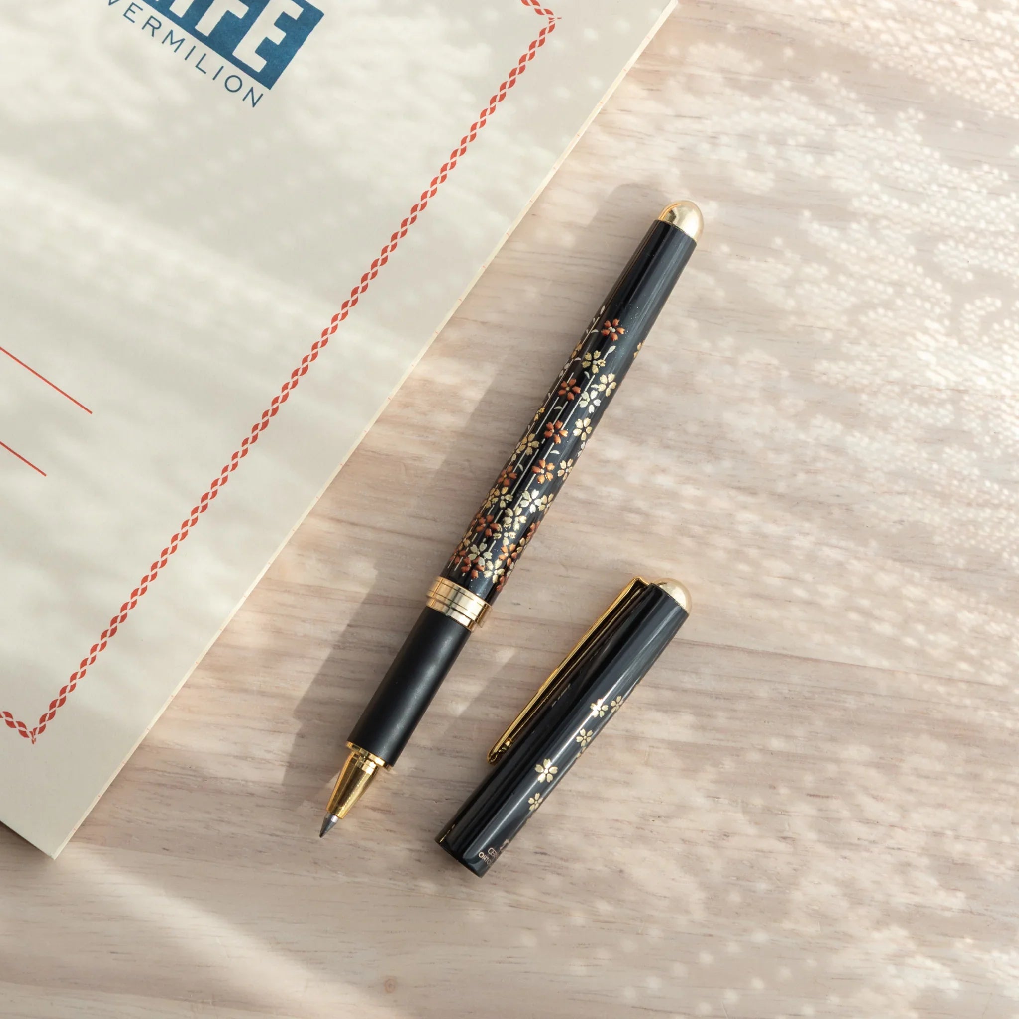 Pink lacquer Yamanaka ballpoint pen features detailed cherry blossom and tree branch design art for writing