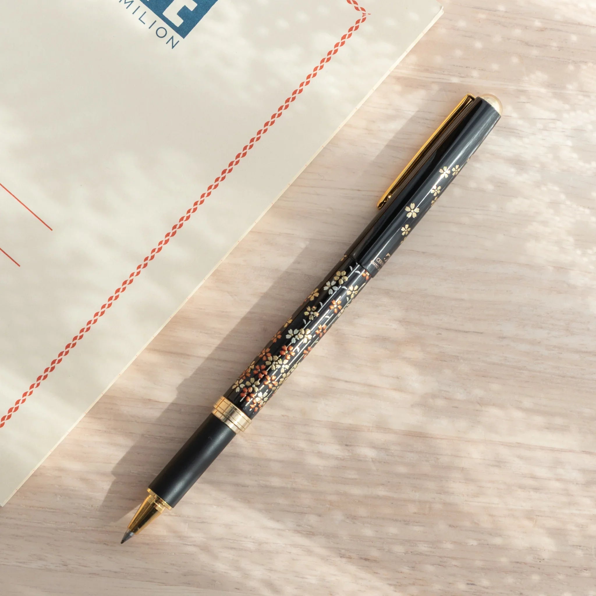 Japanese Ballpoint Pen with detailed Lacquer sakura design and gold accents, cap attached, resting on a desk.