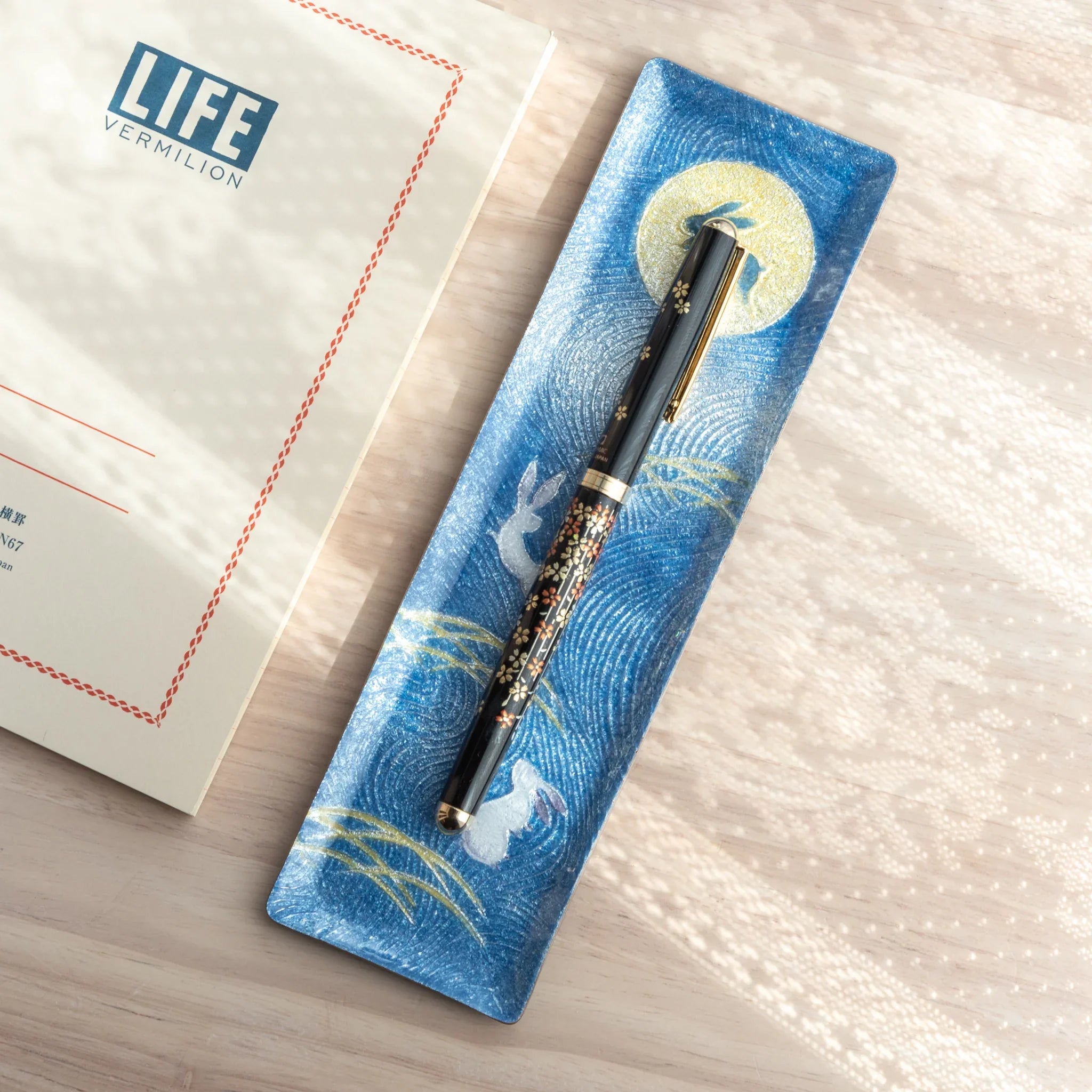 Japanese Ballpoint Pen with a detailed Lacquer sakura design resting on a blue pen tray.