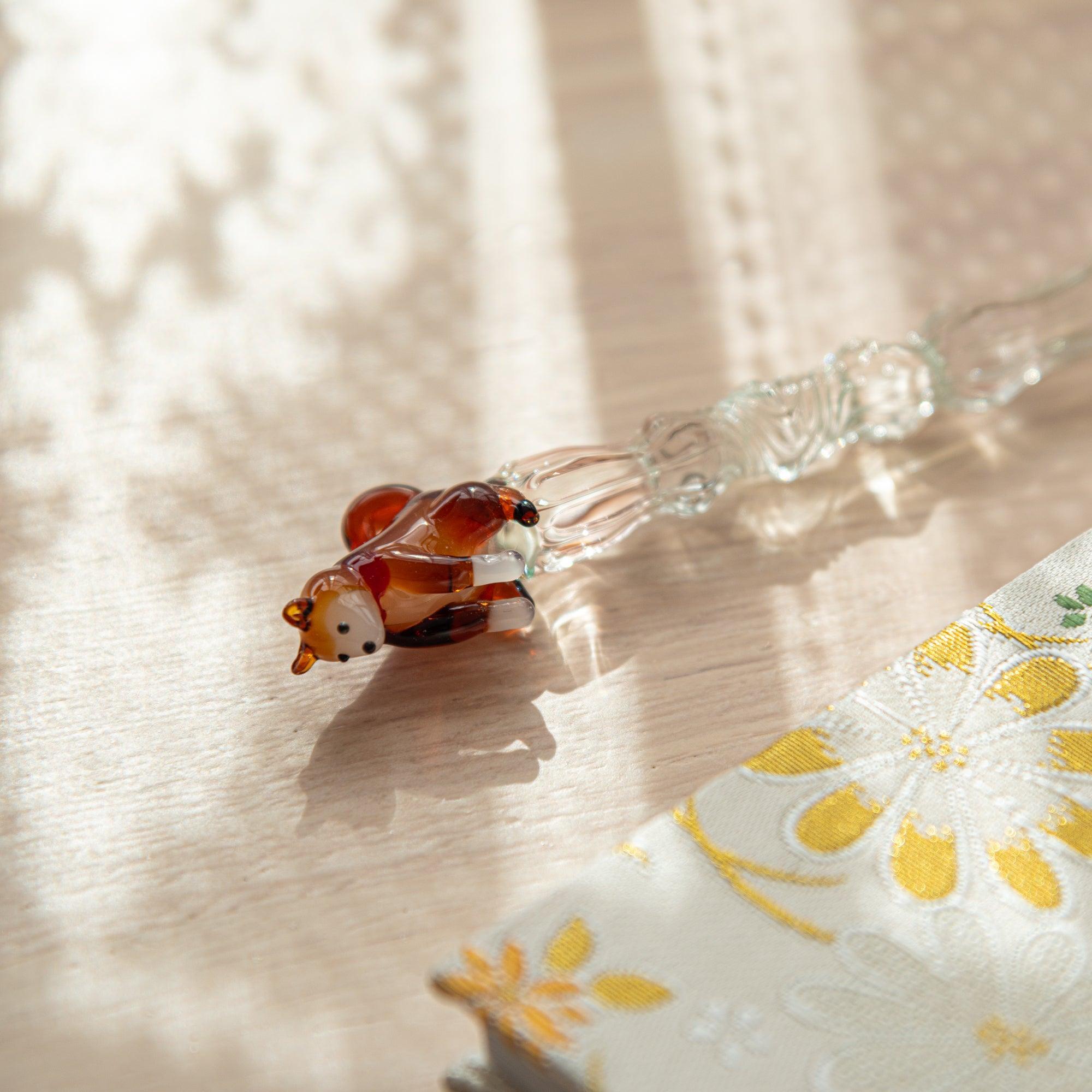 Shiba Inu glass pen with clear light green shaft, resting on a Kyoto Nishijin-ori notebook with floral patterns. Perfect for Japanese stationery lovers.