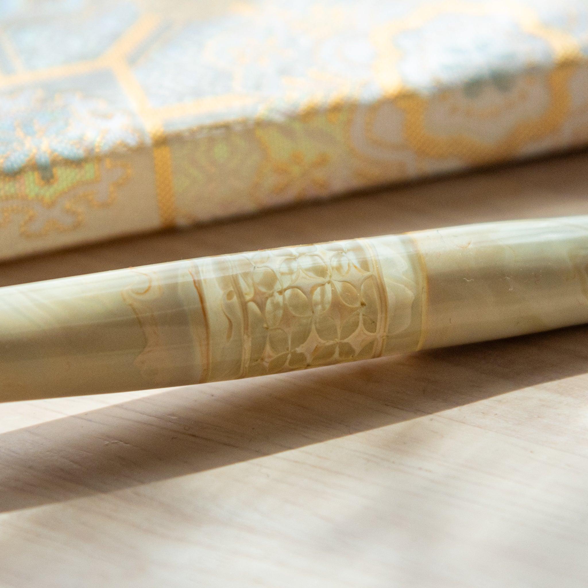 Ivory glass pen with a shippo design, paired with a matching glass pen rest. Displayed on a wooden surface beside a Nishijin textile notebook.