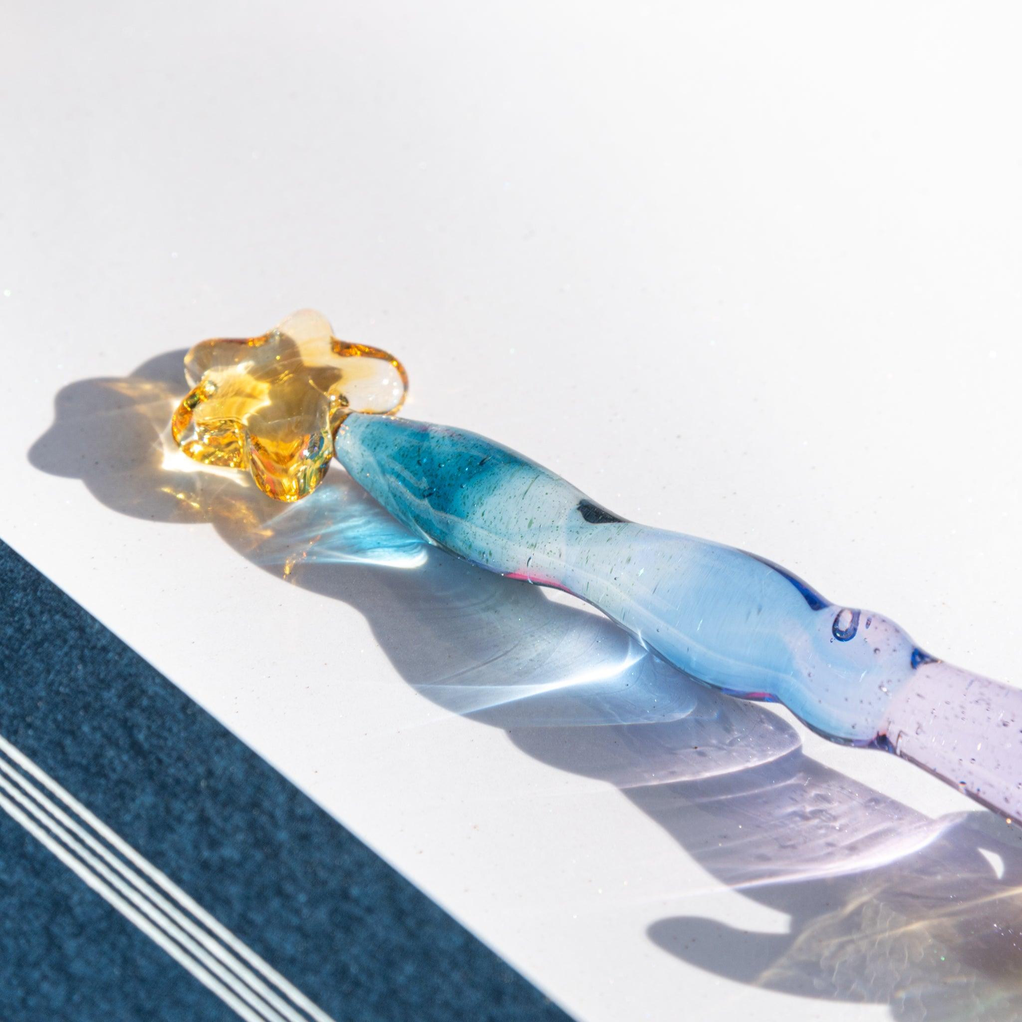 Glass dip pen with a blue-purple gradient body and a gold star-shaped top, casting light reflections on paper.