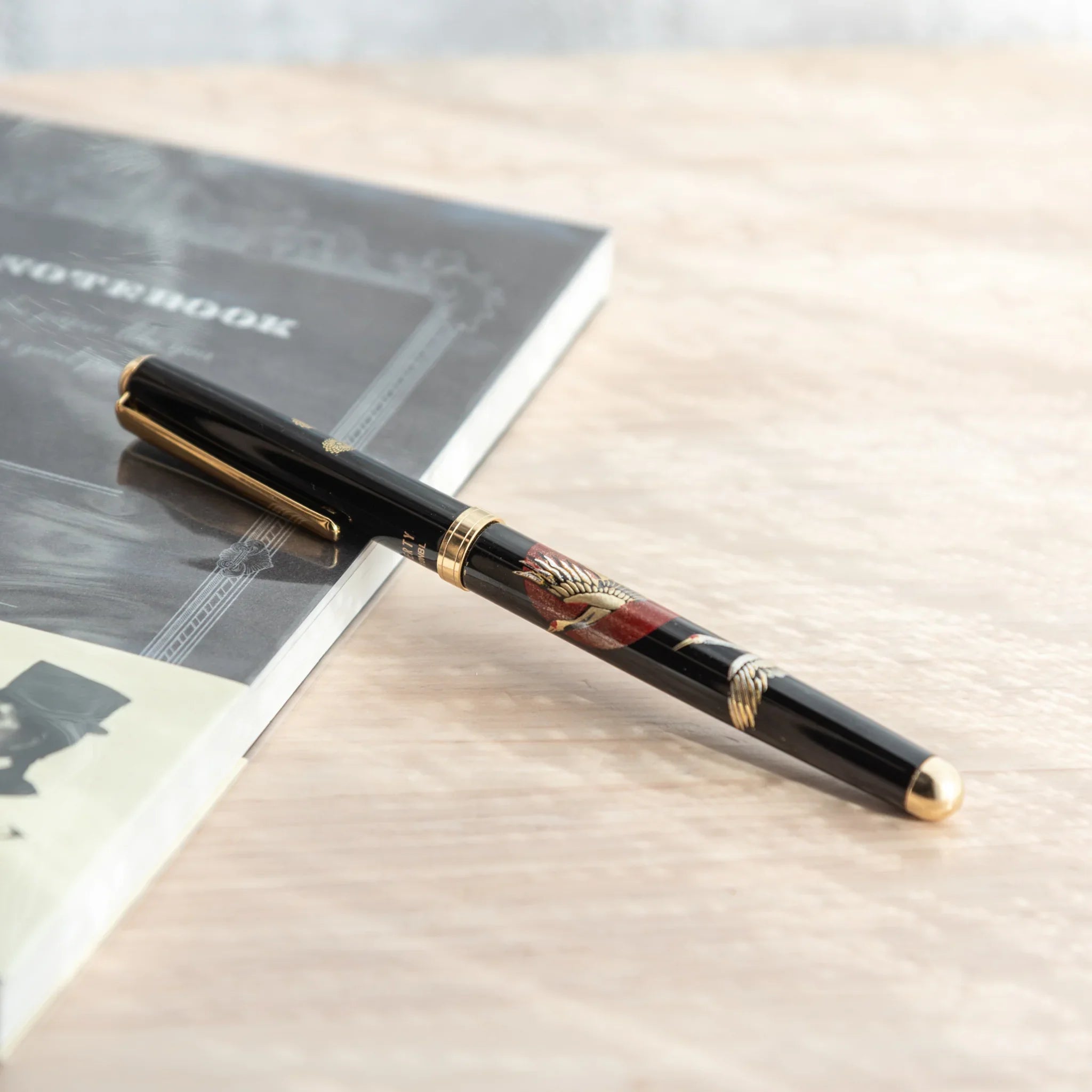 Japanese Ballpoint Pen with crane and red sun Lacquer design, resting on a black notebook.