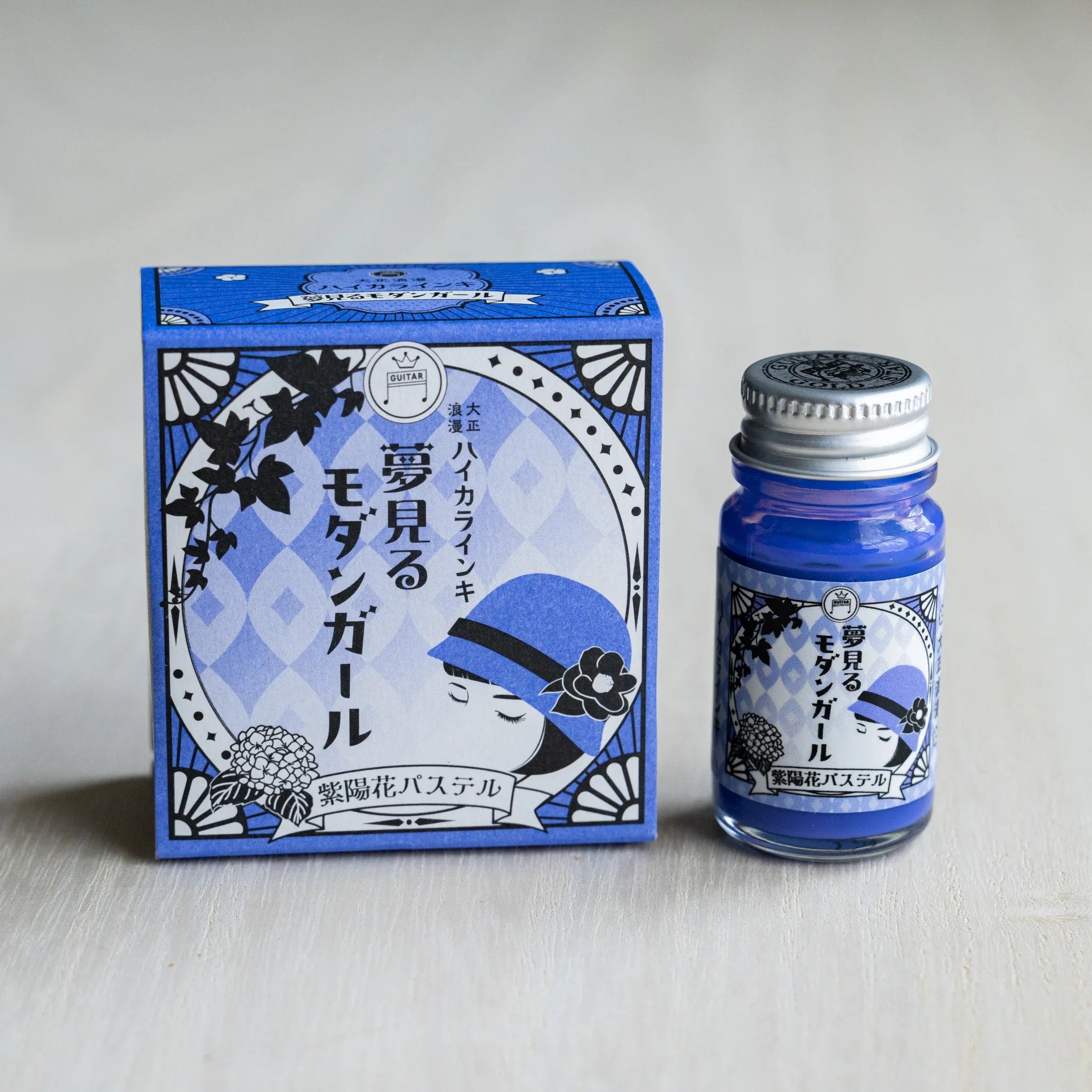 Taisho Romance Hydrangea Pastel ink box in periwinkle blue beside a 12 ml glass bottle of opaque blue violet pigment ink