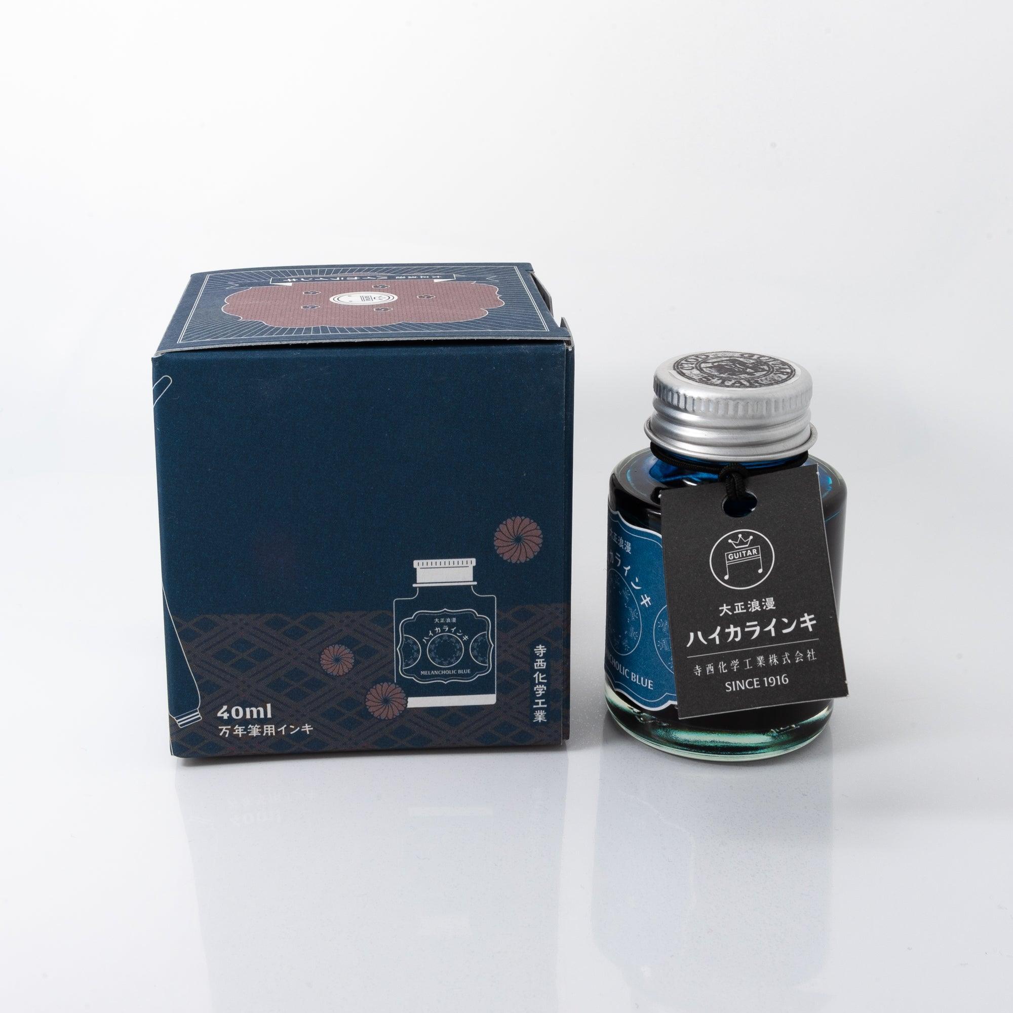 Open Taisho Romance Melancholic Blue ink bottle with vibrant blue liquid, placed beside a fountain pen, blending style and nostalgia.