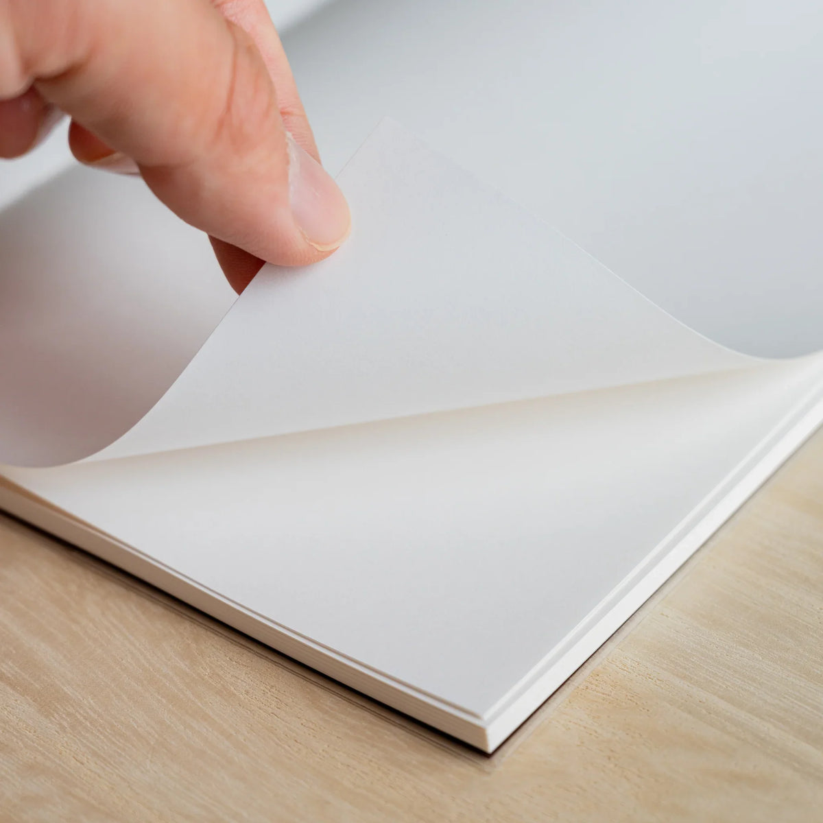 Hand turning a blank white page of the HAIKARA notebook, showing paper thickness and the stacked block of sheets