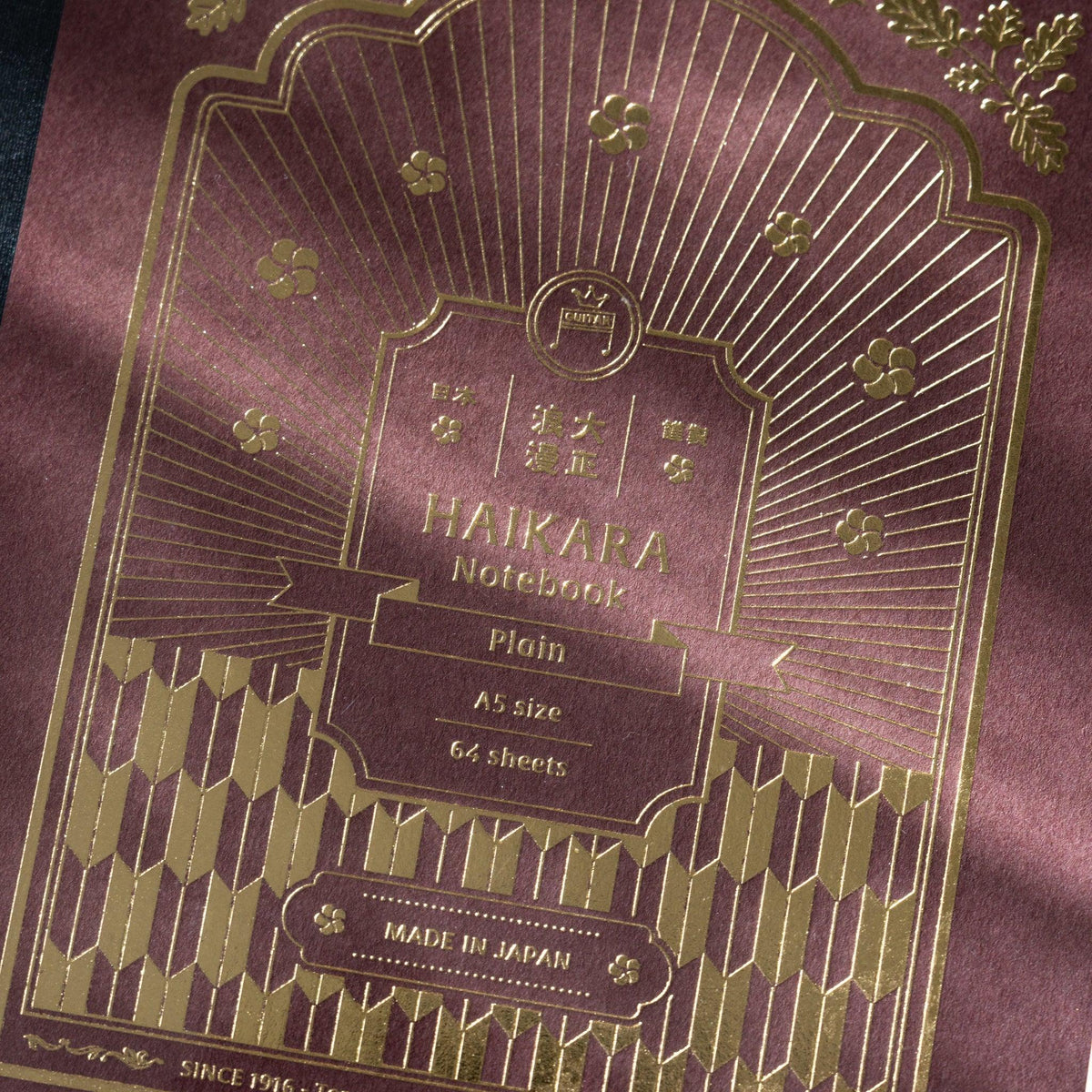 Close-up of gold foil on dark red cover reading HAIKARA Notebook Plain A5 size 64 sheets and Made in Japan