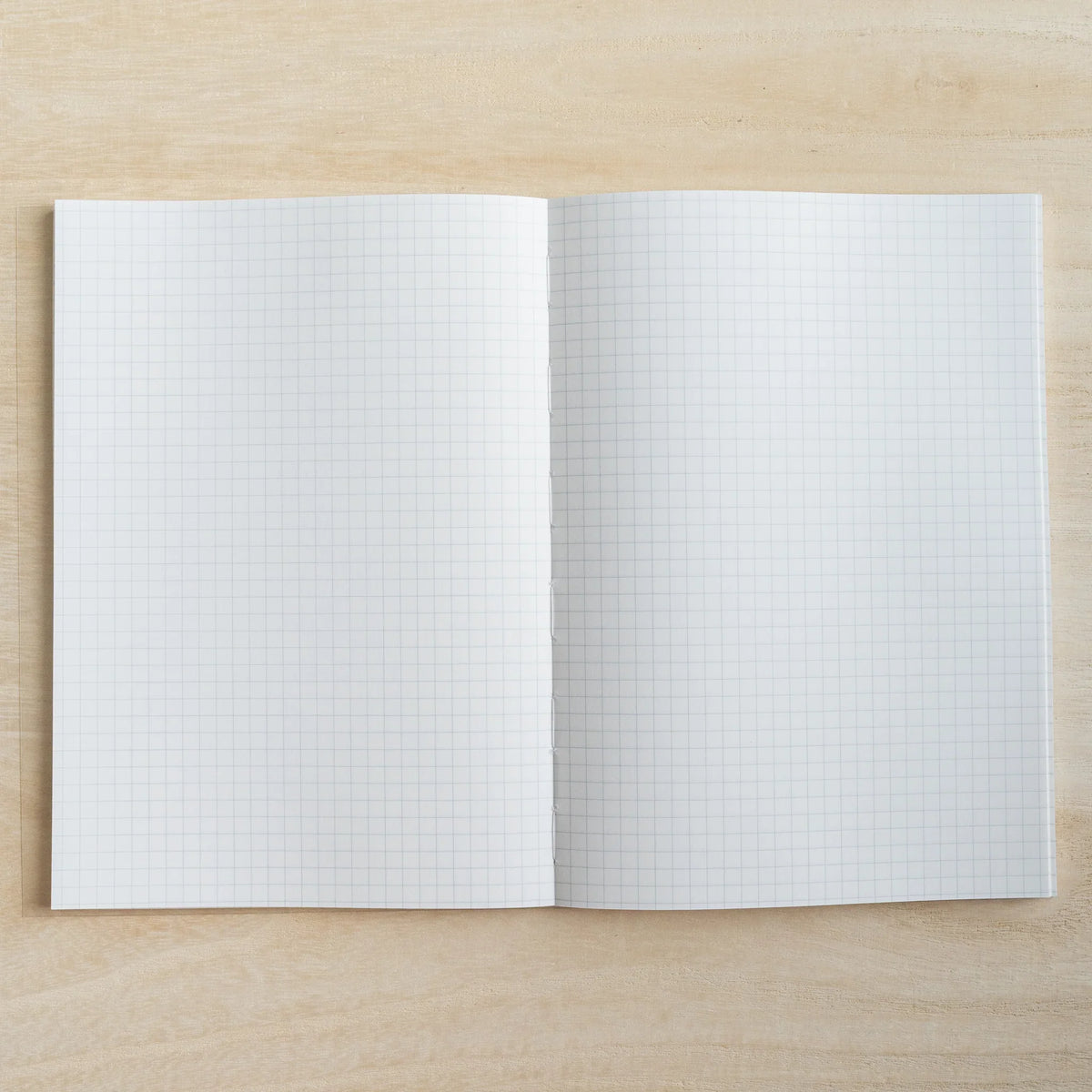 HAIKARA notebook open flat to a grey 5mm grid page spread on a pale wood surface