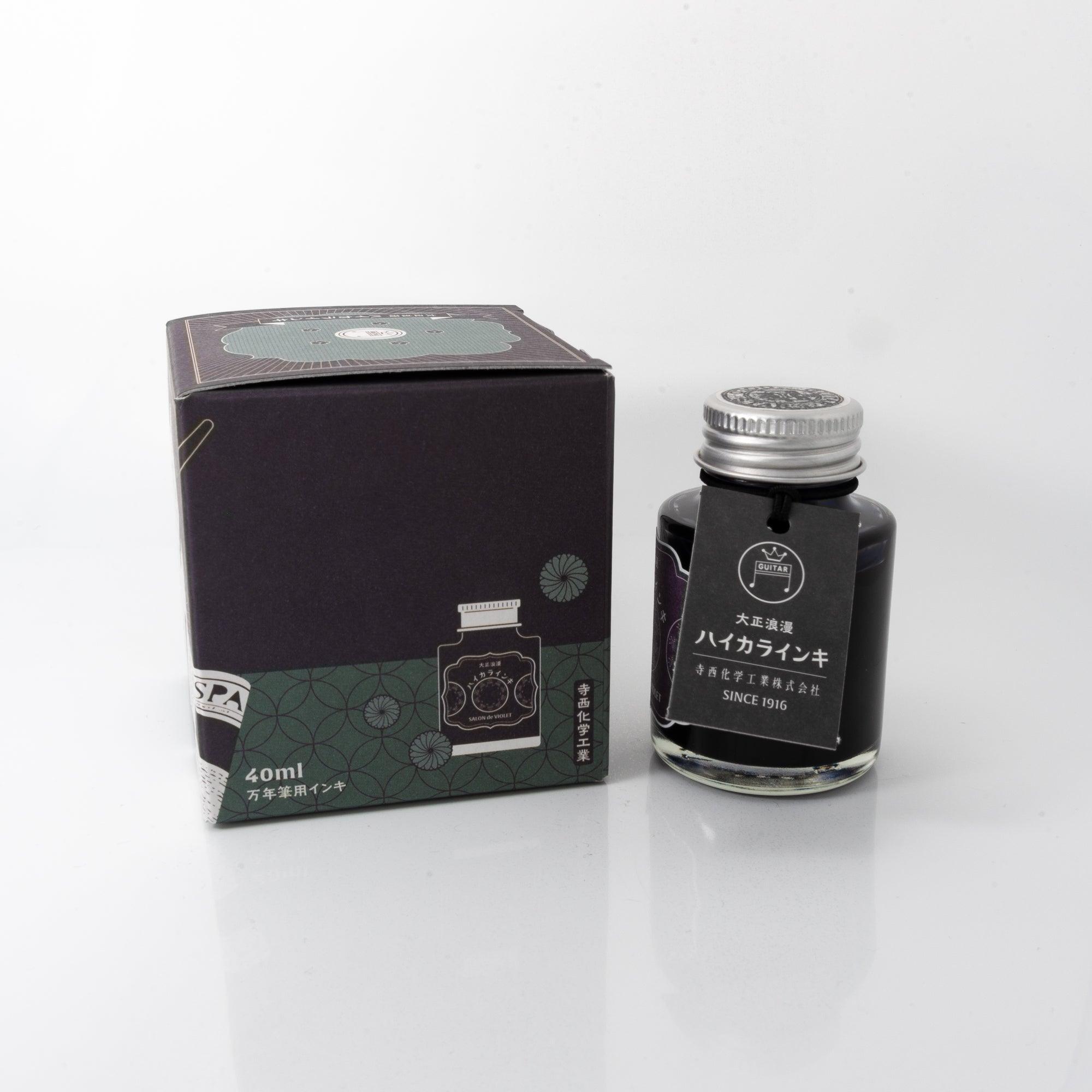 Open Taisho Romance Salon de Violet ink bottle with bold purple liquid, placed beside a fountain pen, blending charm and nostalgia.