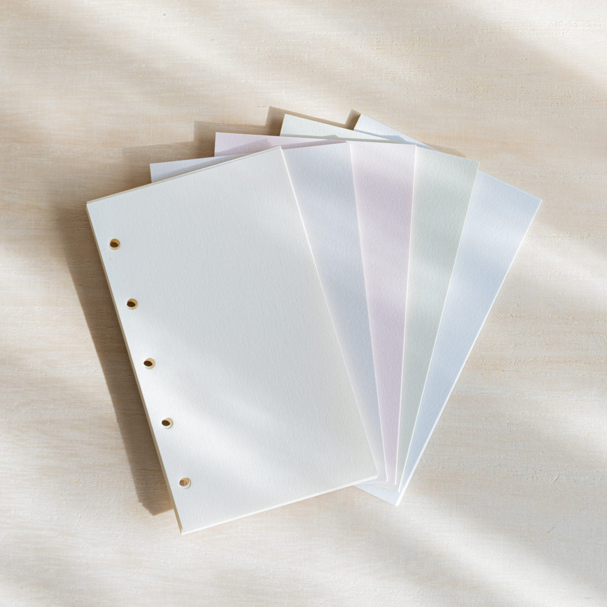 Five Araveal M5 refill sheets fanned out in natural, ash gray, primrose, sage green and slate blue with punched holes