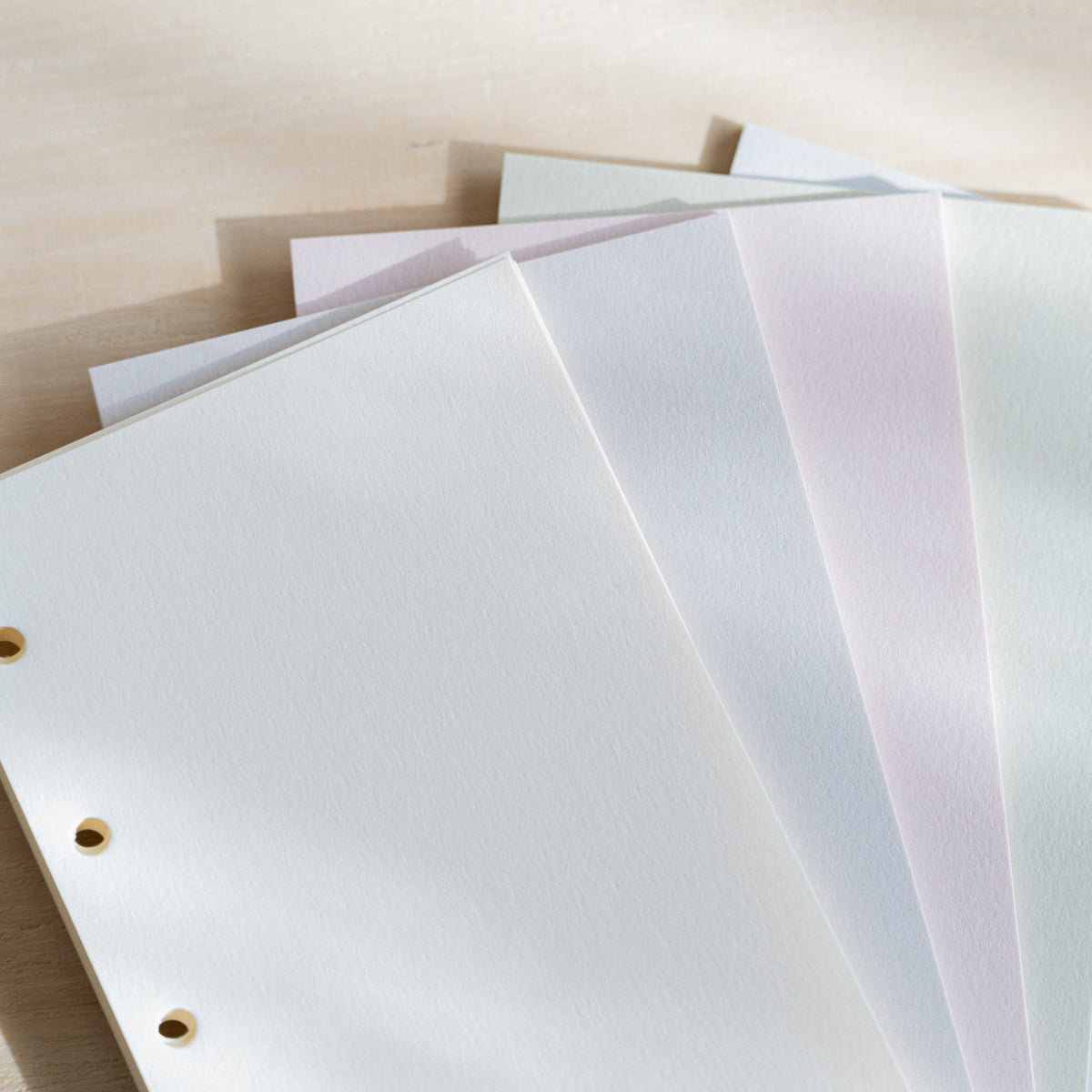 Close-up of fanned Araveal refill sheets in five pale colors with a matte paper surface and punched holes