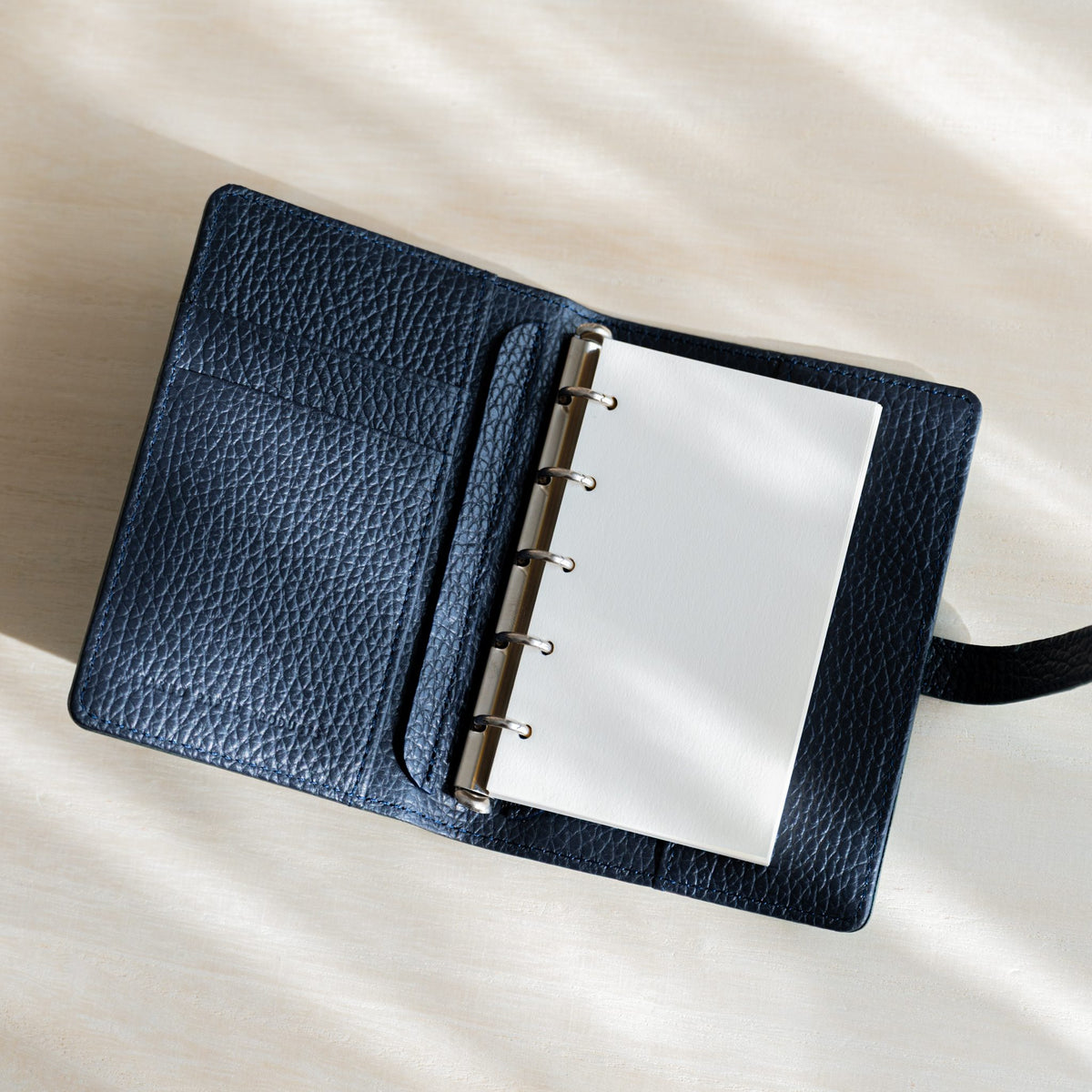 Araveal M5 refill sheets on the silver rings of an open navy grained leather planner with card pockets