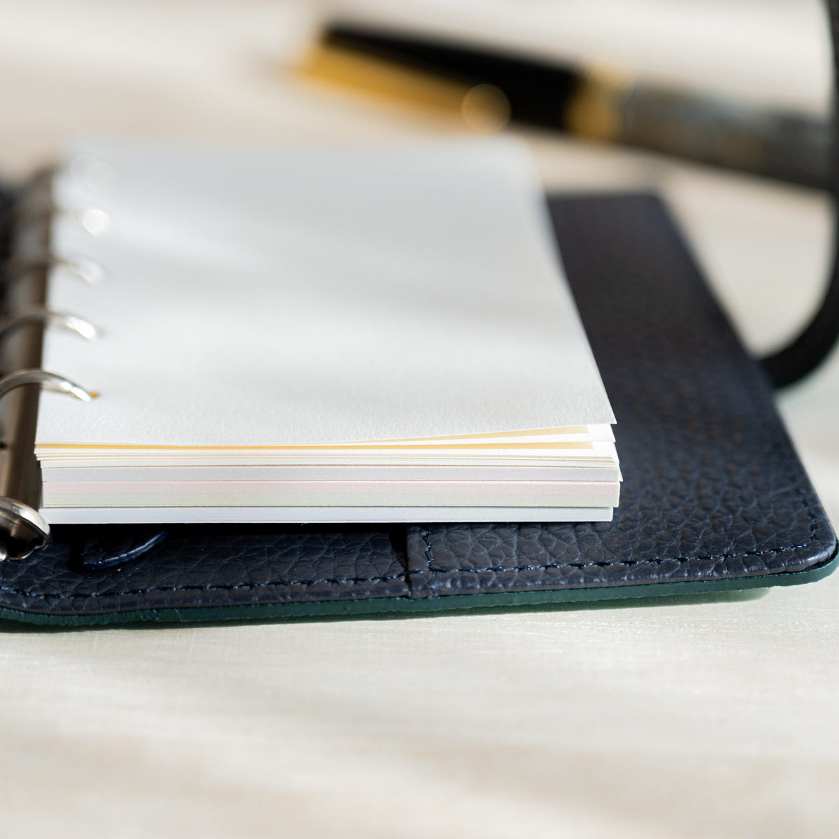 Stack of Araveal M5 refill sheets on planner rings showing the layered pastel edges of the five colors