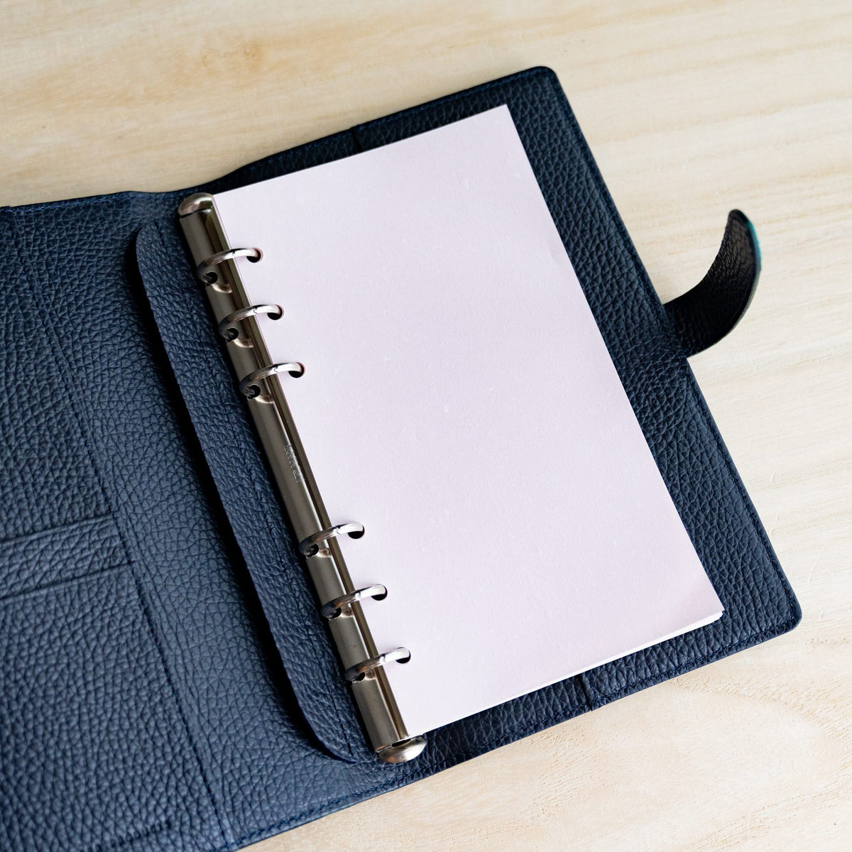 Pale pink Feather Waltz Bible refill on the rings of an open navy planner with a snap strap
