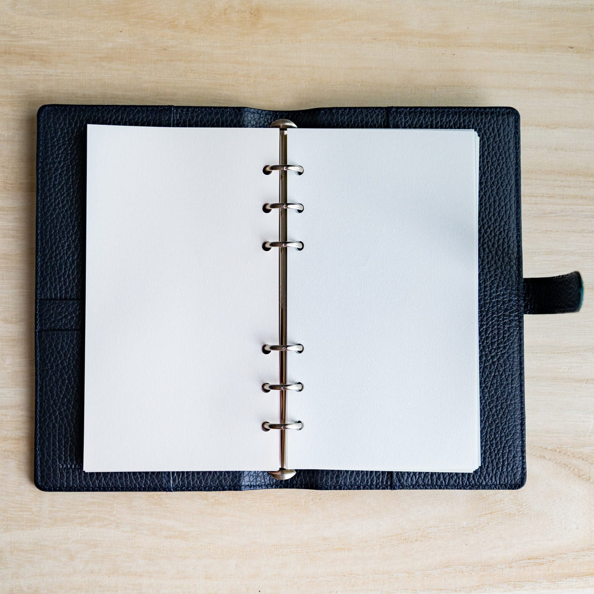 White Feather Waltz Bible refill sheets on the silver rings of an open navy grained leather planner