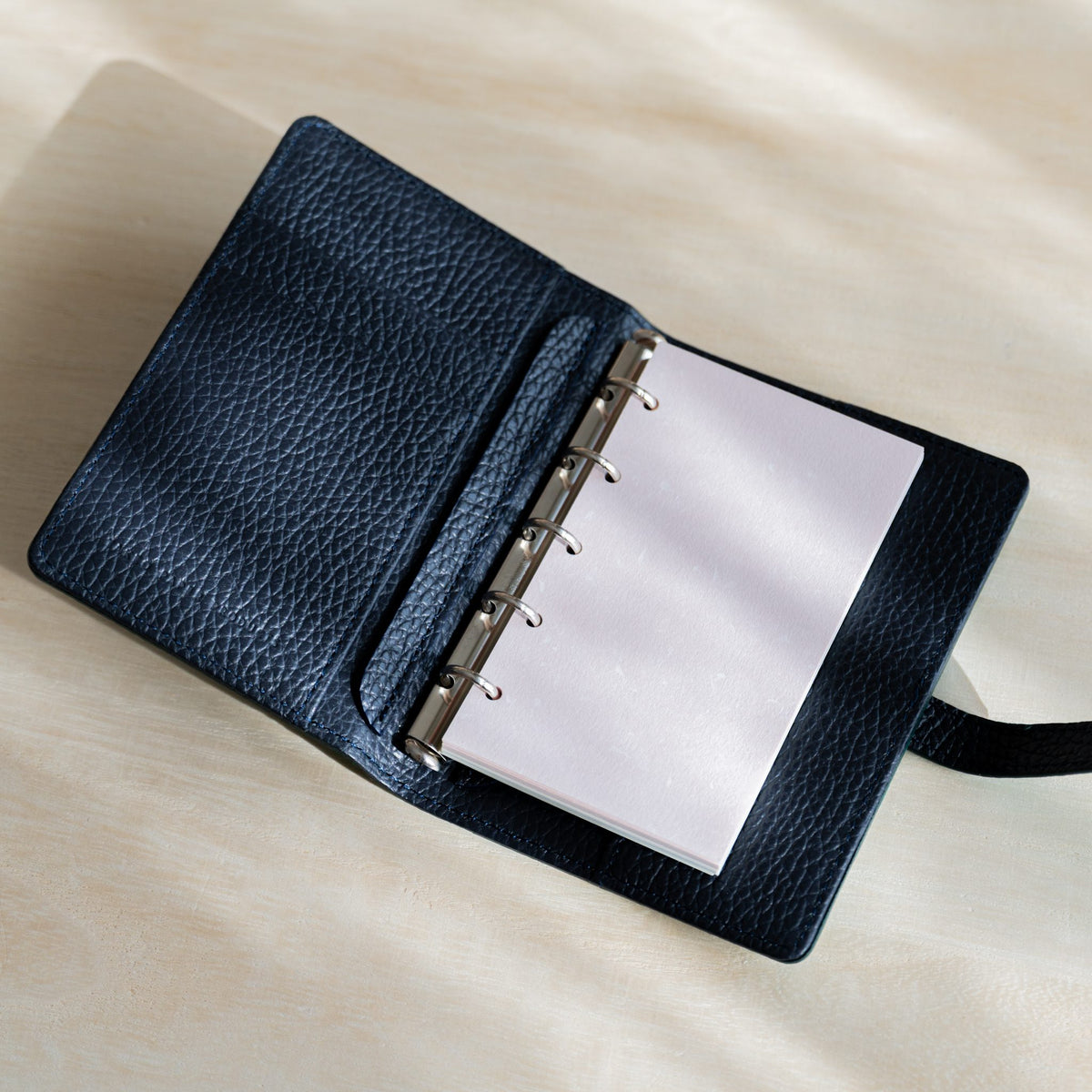 Pale pink Feather Waltz M5 refill on the silver rings of an open navy grained leather planner