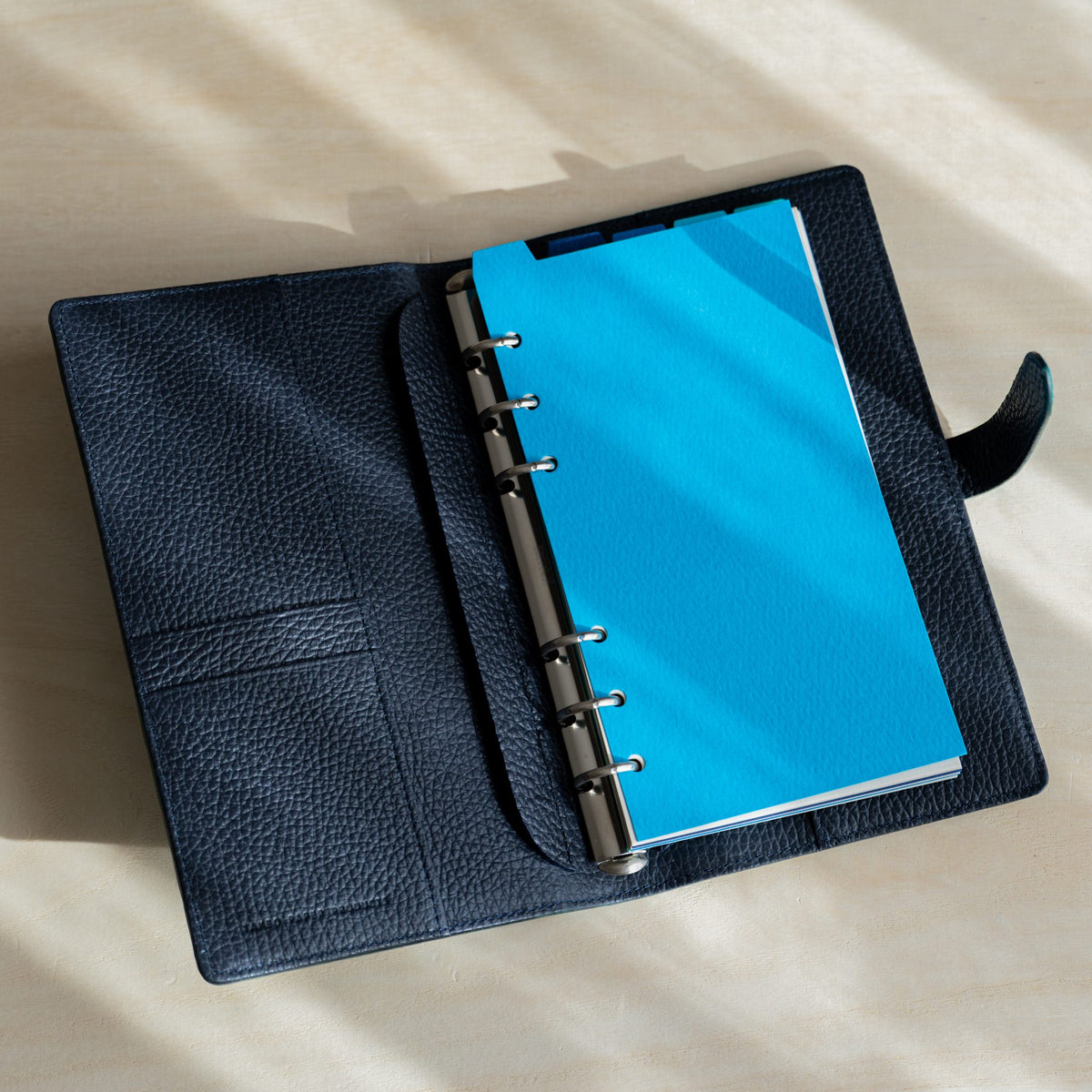 Mermaid Assorted Blues divider on the rings of an open Ise Gikakushi Bible planner with navy leather interior