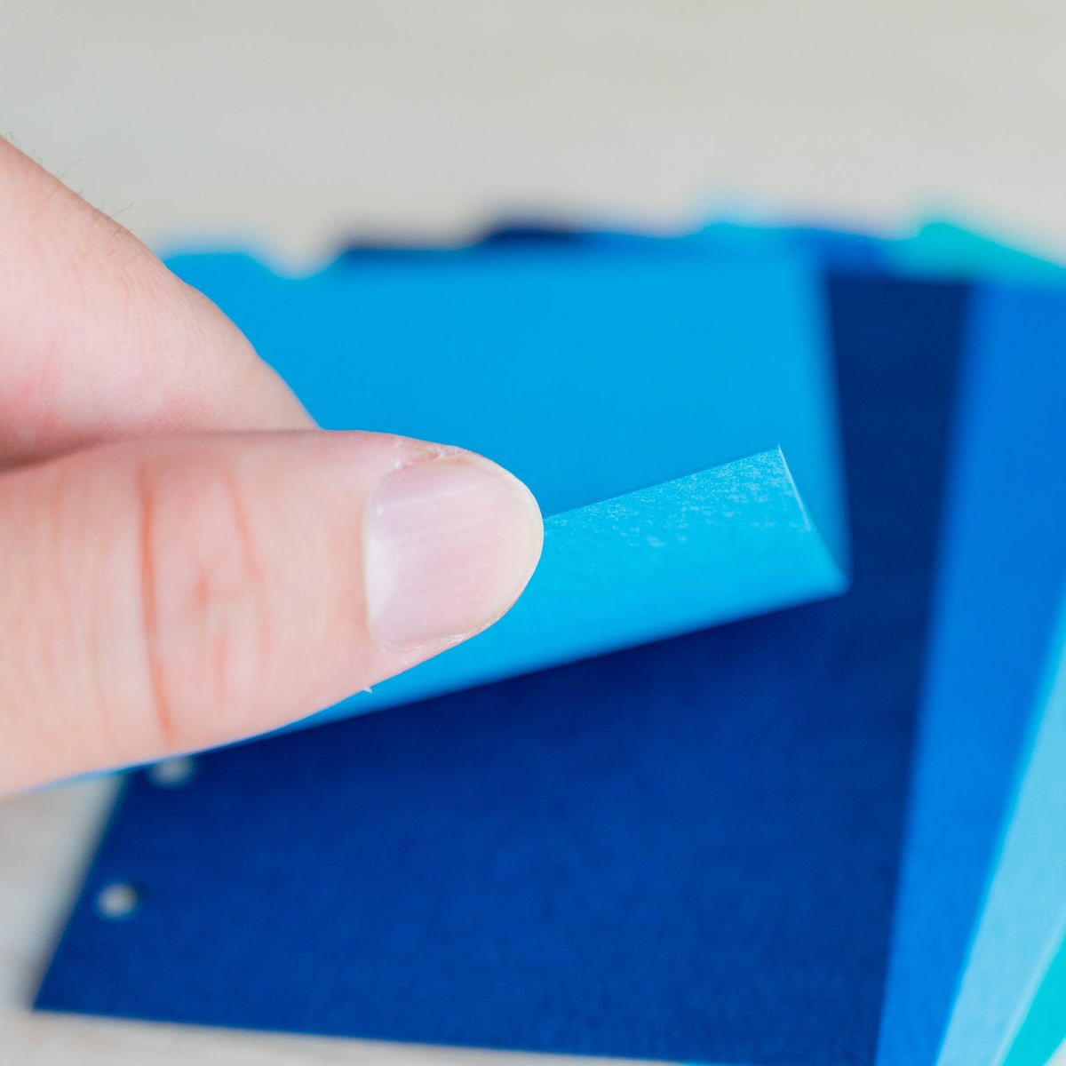 Fingertip lifting the corner of a sky blue Mermaid Mini 6 divider over cobalt sheets