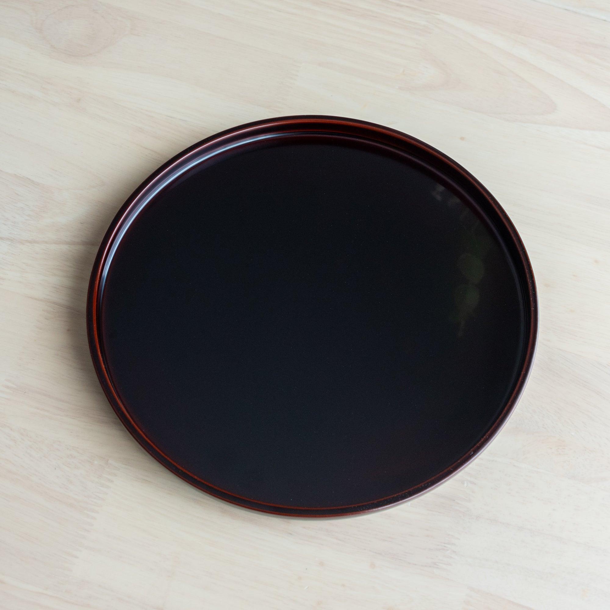 A simple, glossy black Japanese stationery lacquered tray with a red rim, placed on a wooden table.