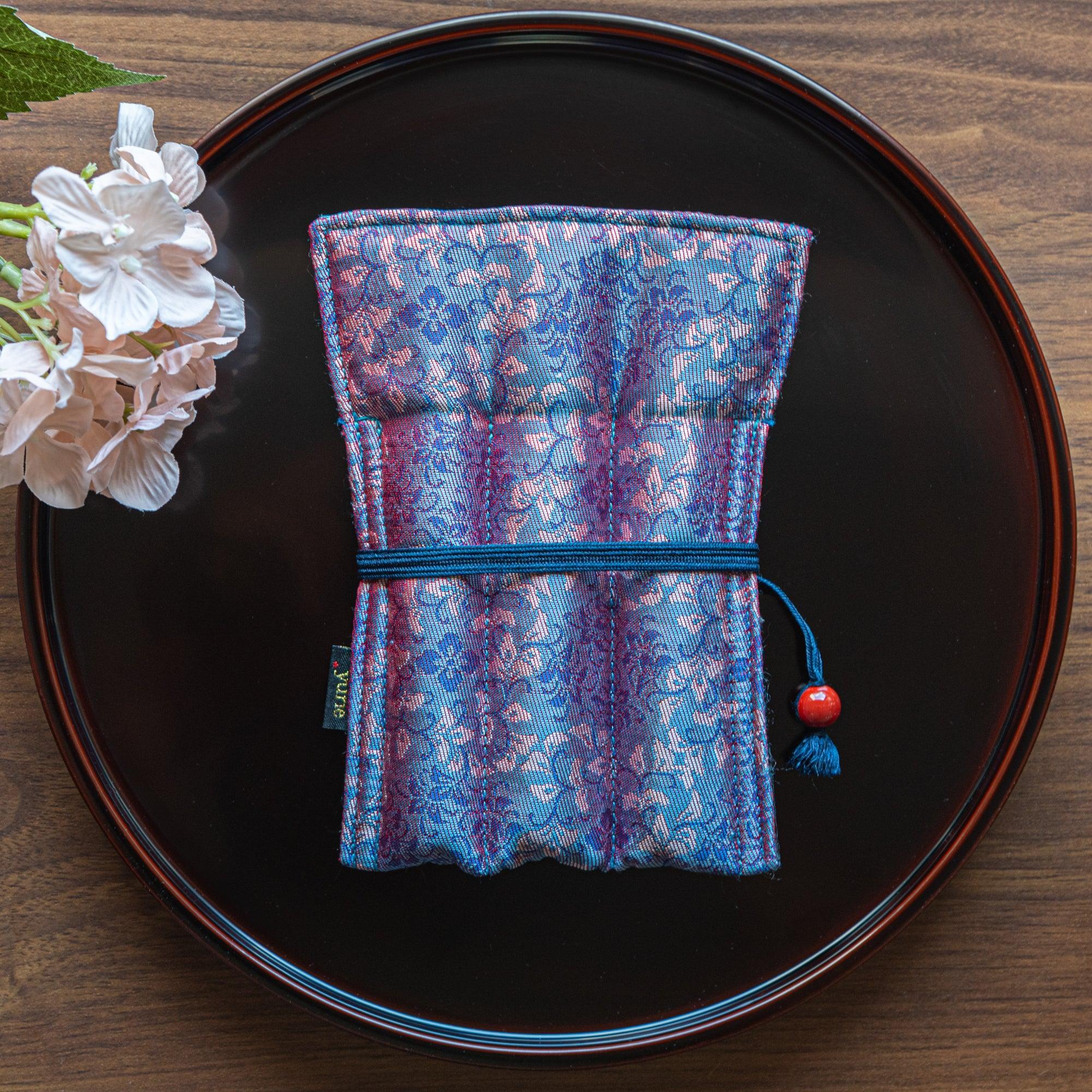 A Japanese stationery pen case in a purple and blue floral brocade design, placed on a black lacquered tray with hydrangea accents.