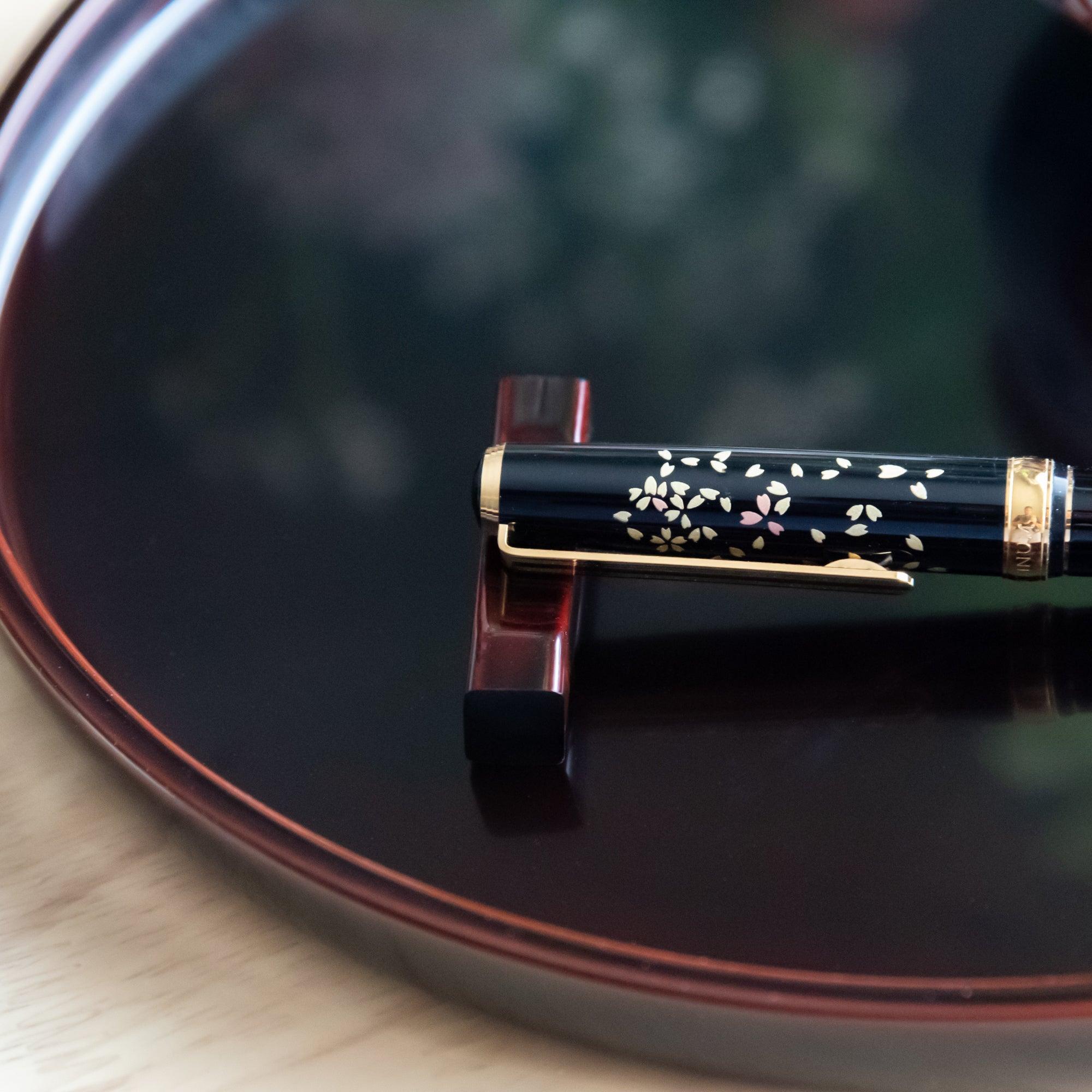 A detailed shot of a sakura-designed fountain pen, a Japanese stationery item, placed on a red pen rest over a black lacquer tray.
