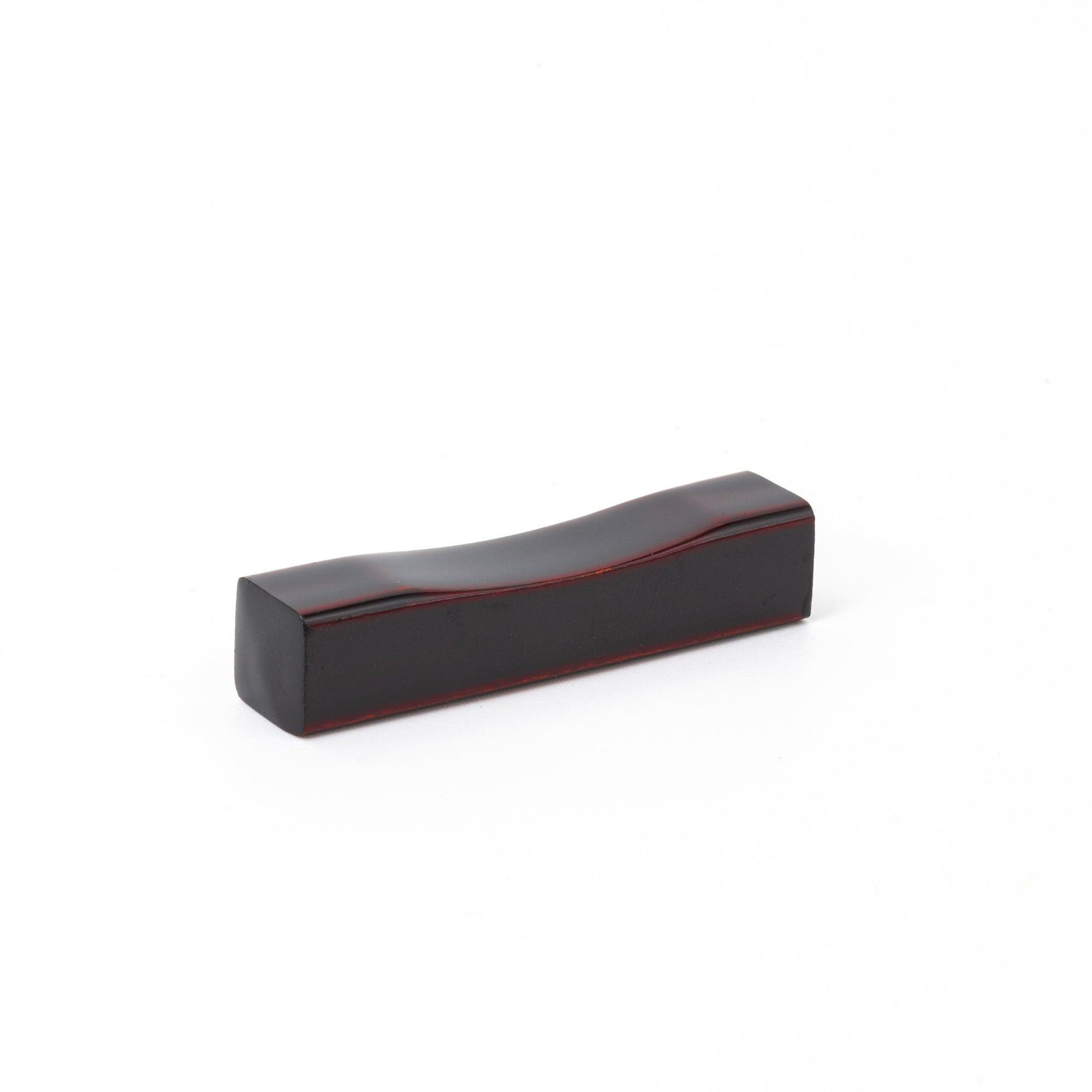 A single Japanese stationery pen rest in deep red with a curved design against a white background.