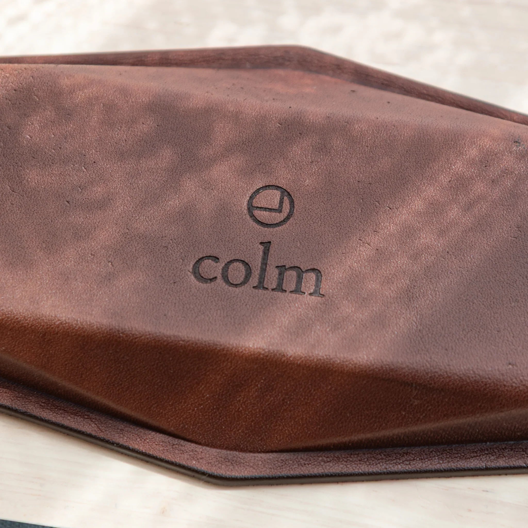 Brown leather hexagonal pen tray base with embossed colm logo and geometric outline, showing leather texture and hex shape