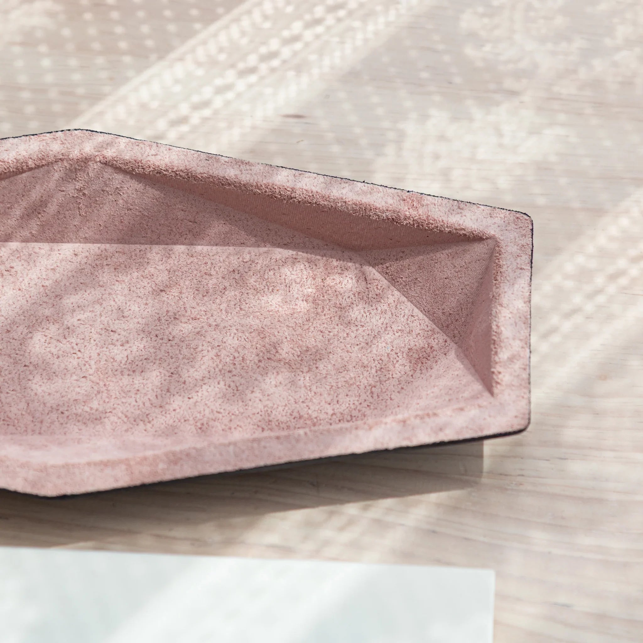 Empty pink suede hexagonal pen tray interior from an angle showing geometric wall panels and suede texture, black leather rim