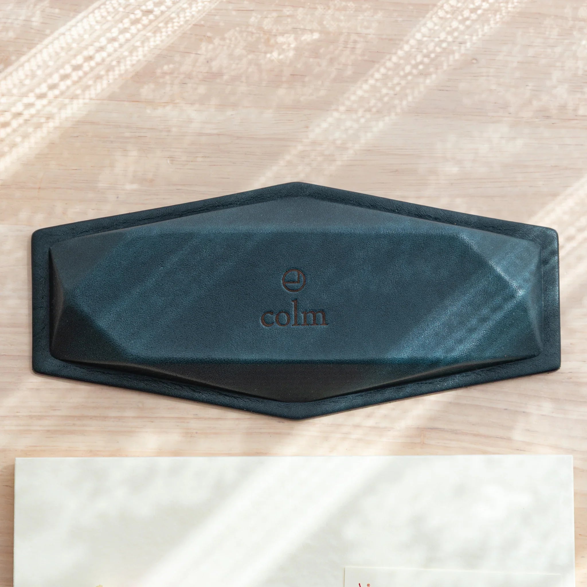 Blue-gray suede hexagonal slim pen tray flipped upside down showing dark teal suede base with embossed colm logo
