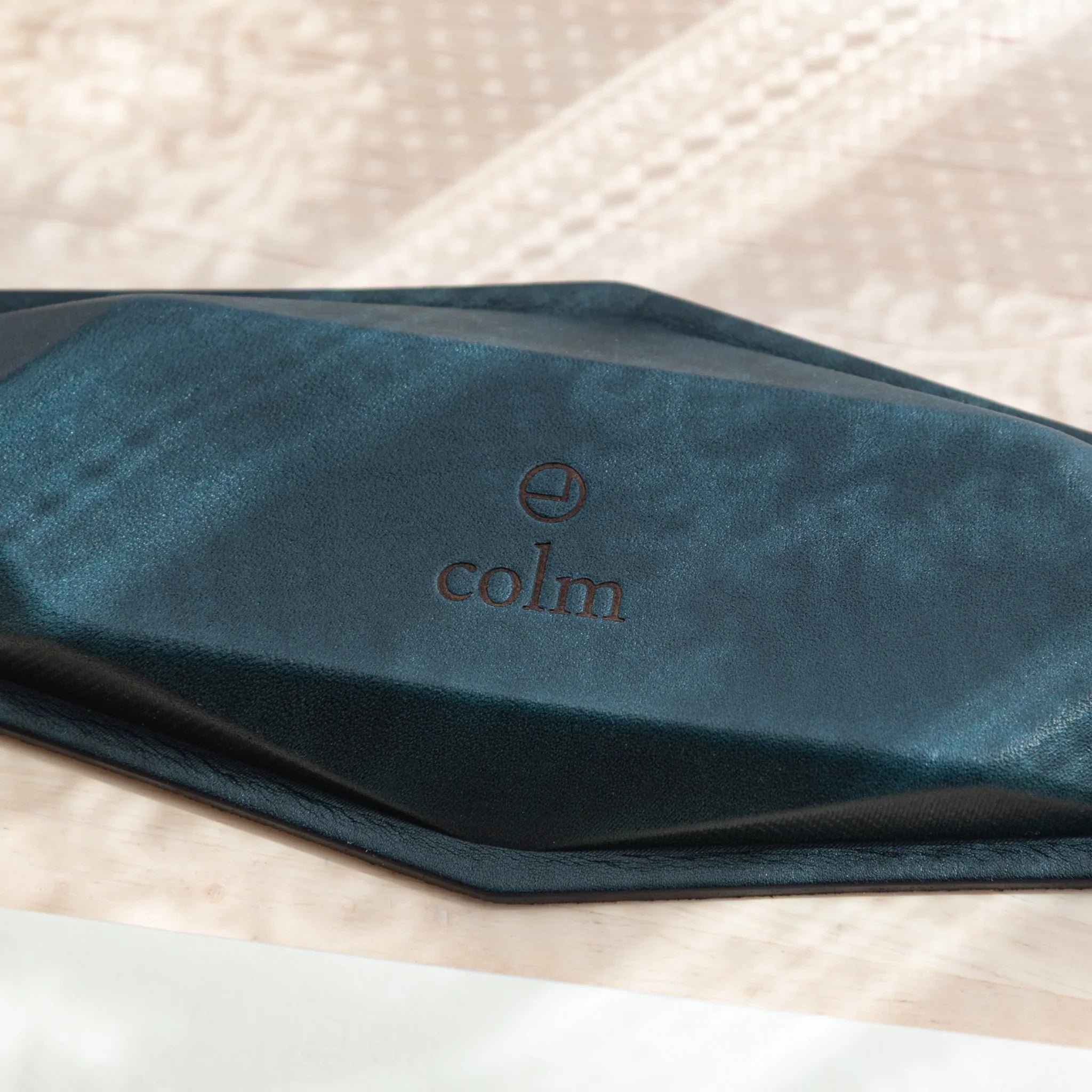 Close-up of dark teal suede pen tray base with embossed colm logo and black leather edge showing geometric hexagonal outline
