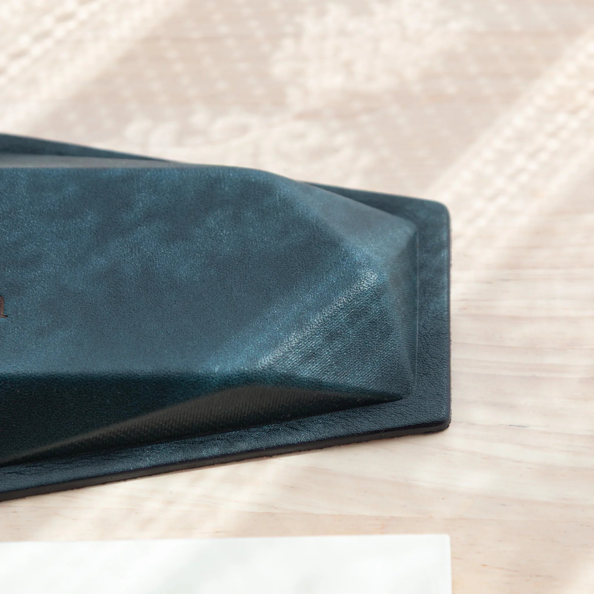 Corner detail of dark teal suede pen tray base showing suede texture, geometric angled corner, and black leather border