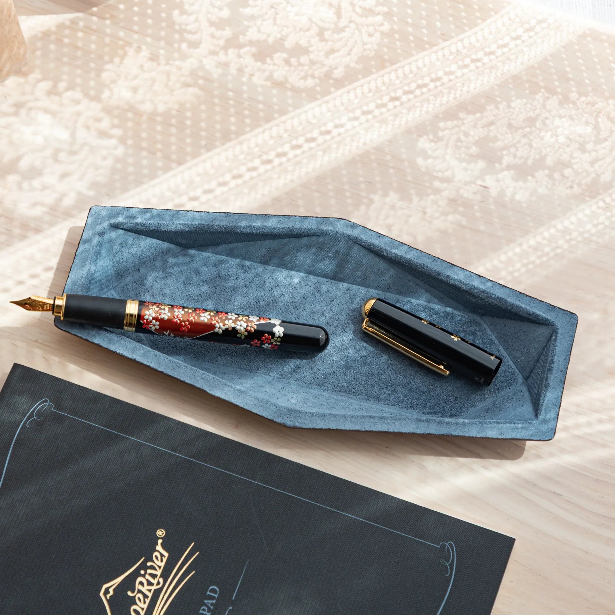 Blue-gray suede hex slim pen tray with uncapped Japanese fountain pen and cap placed beside it, on a navy writing pad
