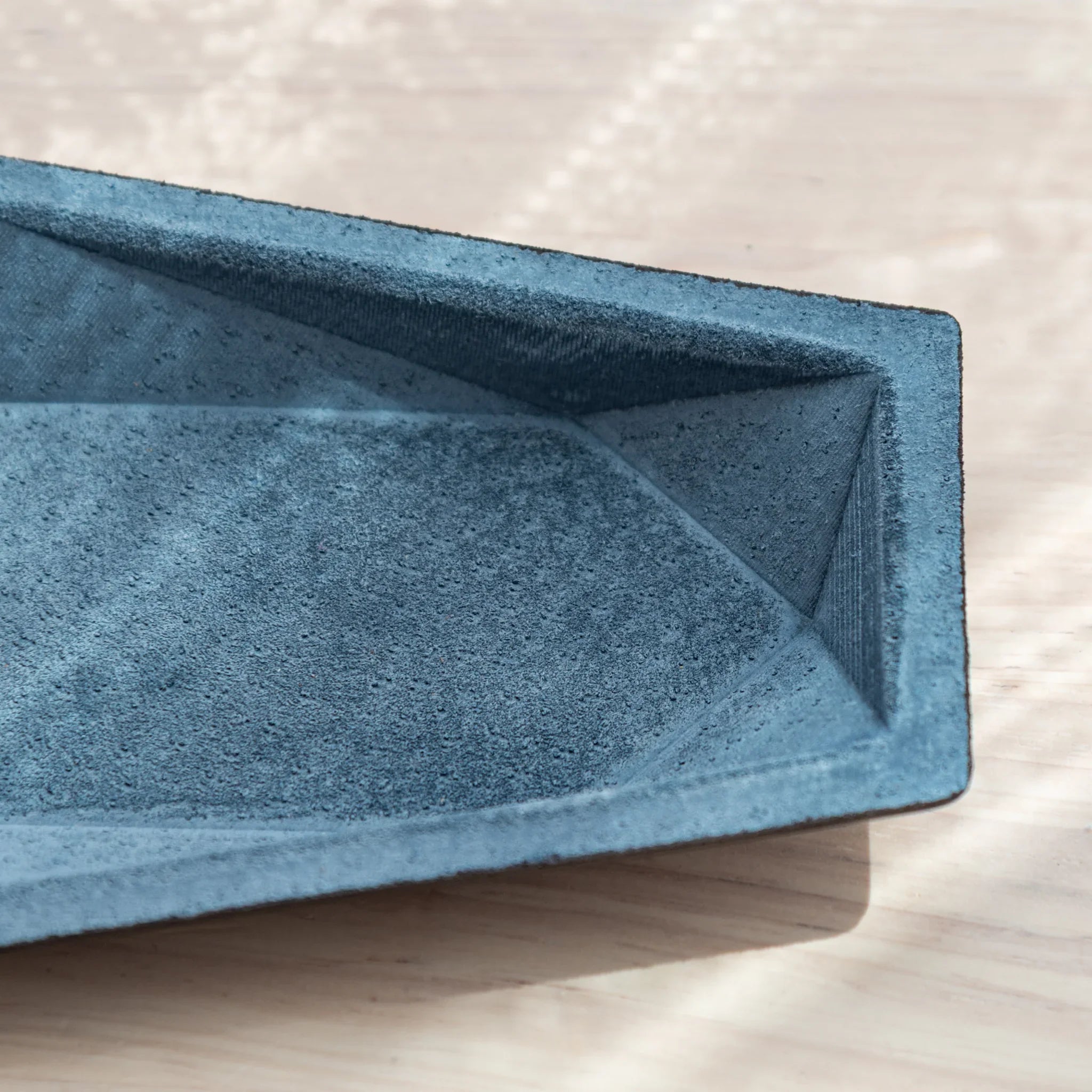 Empty blue-gray suede hexagonal pen tray interior showing angled geometric walls and suede texture with black leather rim