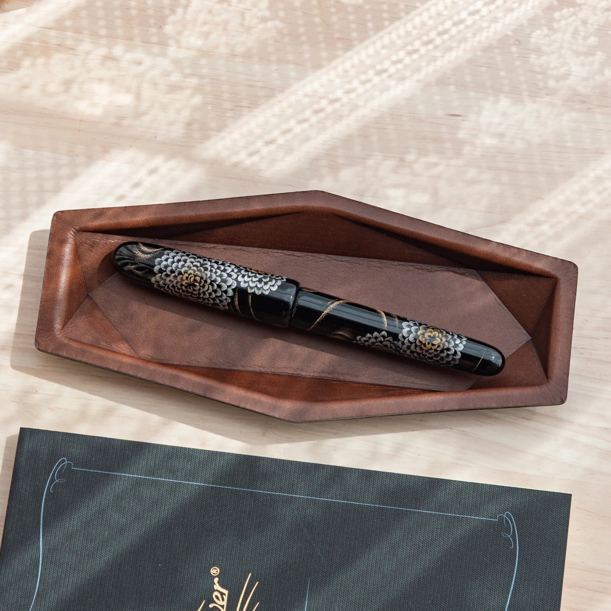 Overhead view of tan leather hexagonal pen tray with decorative black-patterned fountain pen resting securely inside