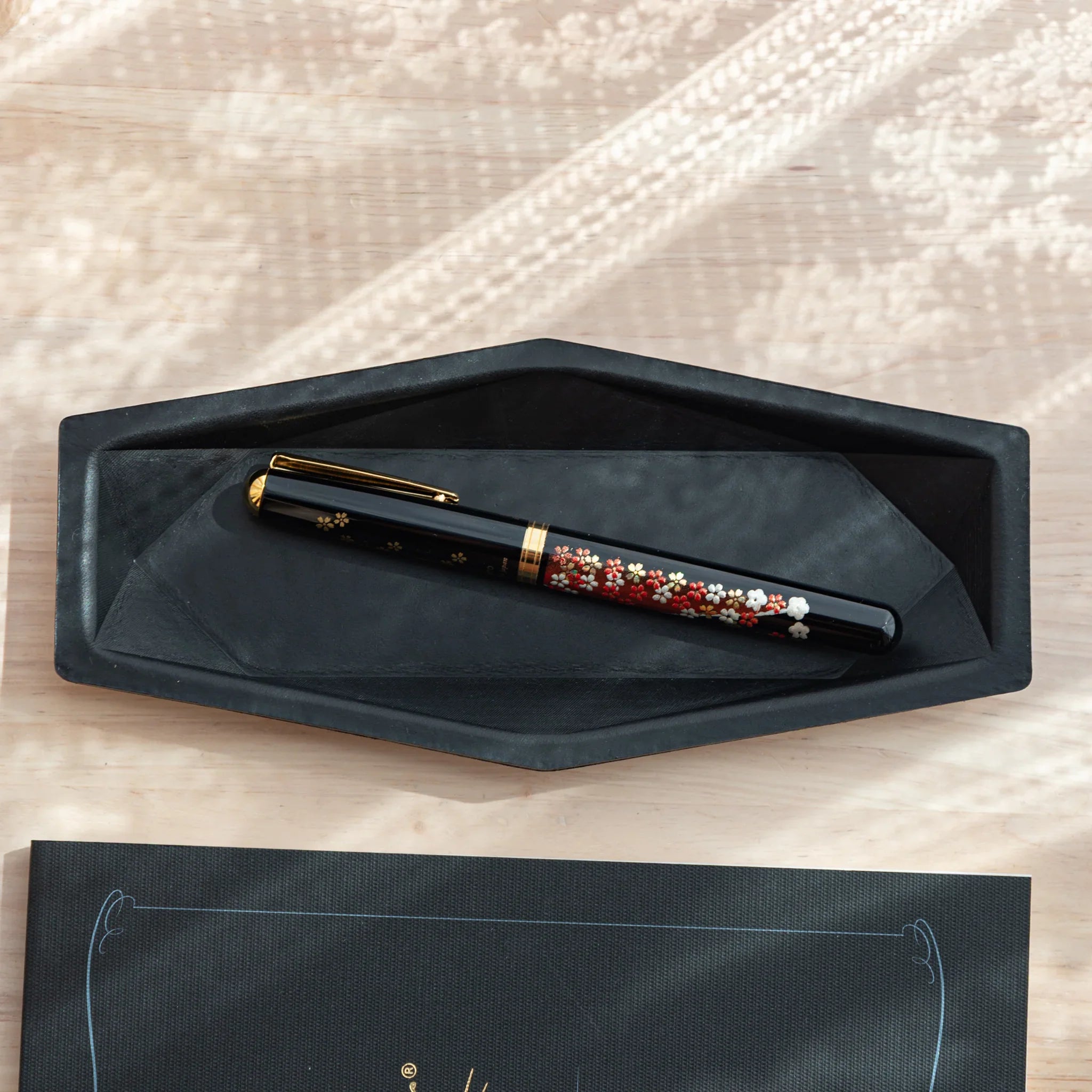 Black leather Japanese Pen Tray holding a floral lacquer fountain pen.