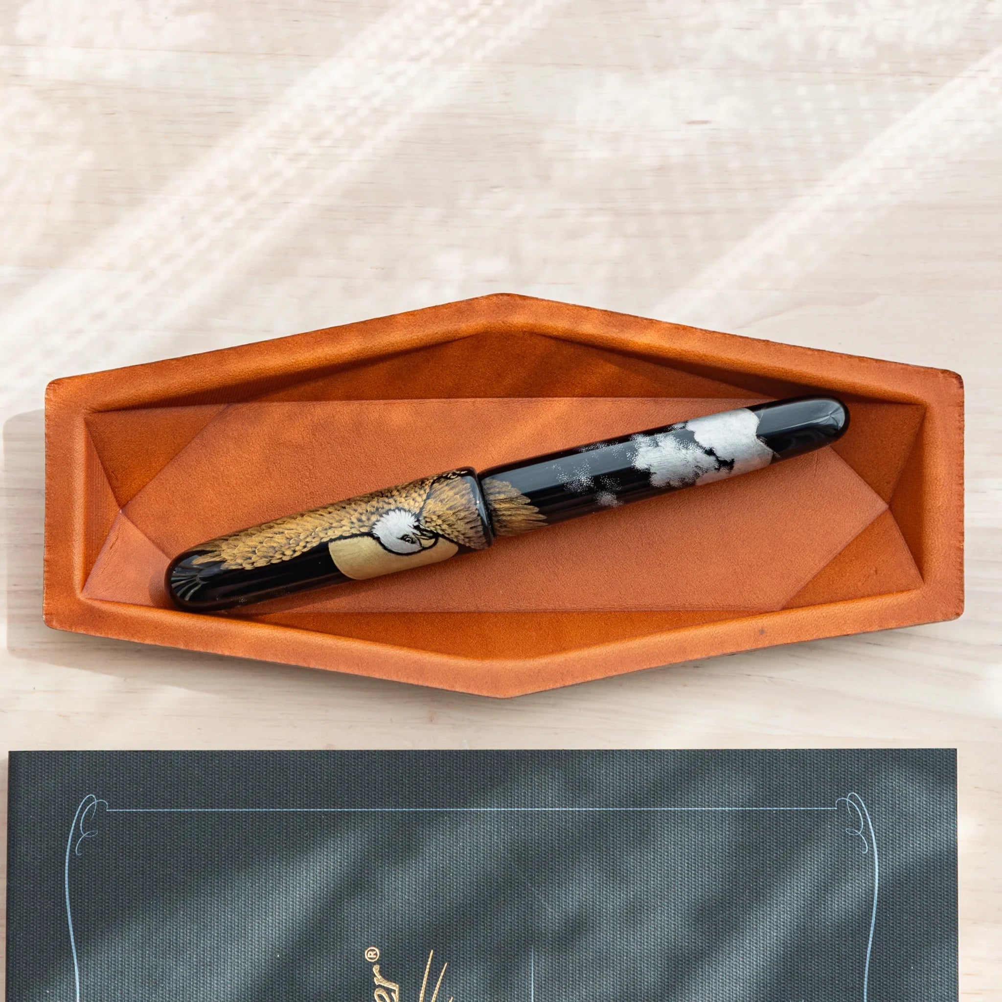 Overhead view with a single decorative fountain pen resting in the center of the tan leather pen organizer tray