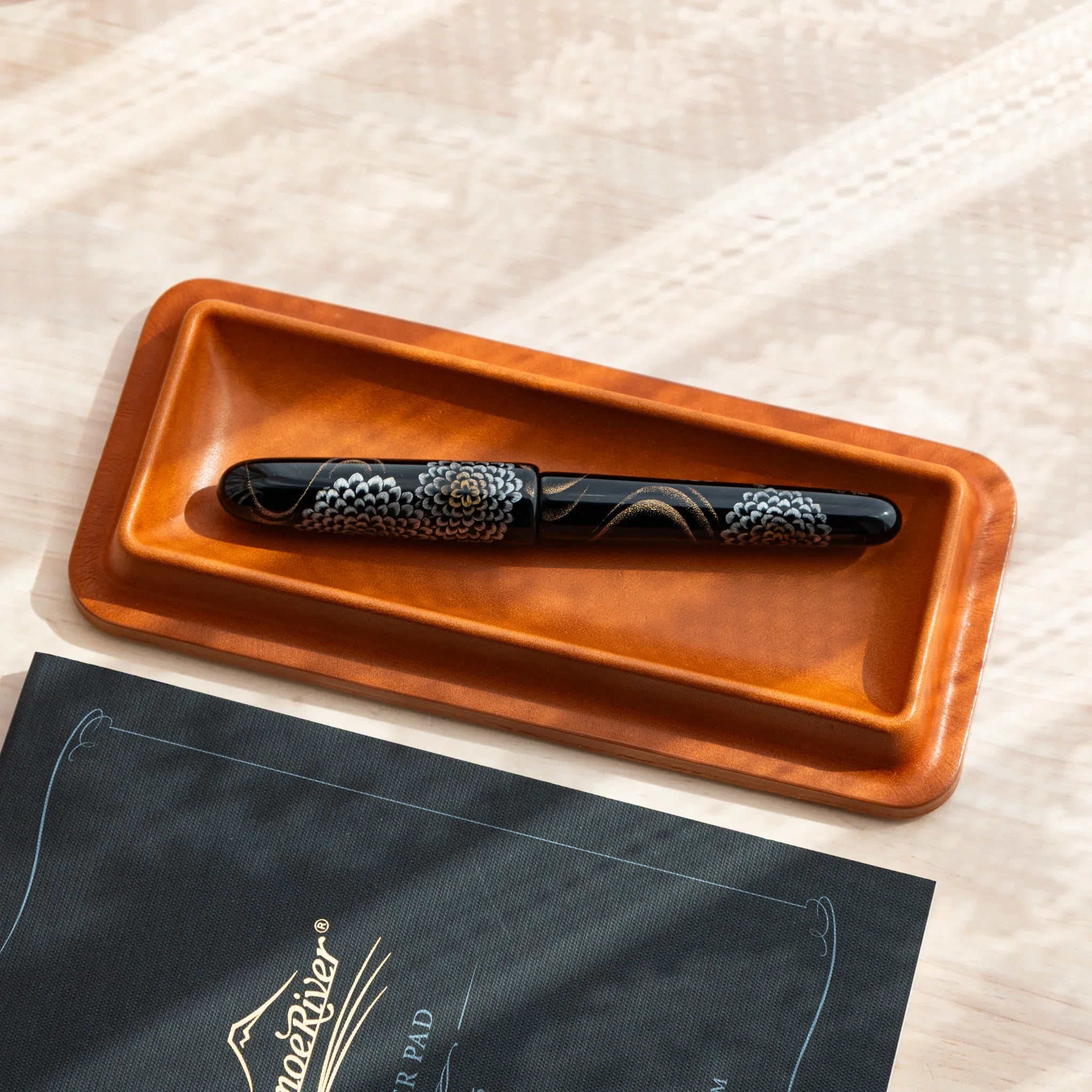 Tatsuno leather pen tray holding a Japanese fountain pen with floral maki-e design