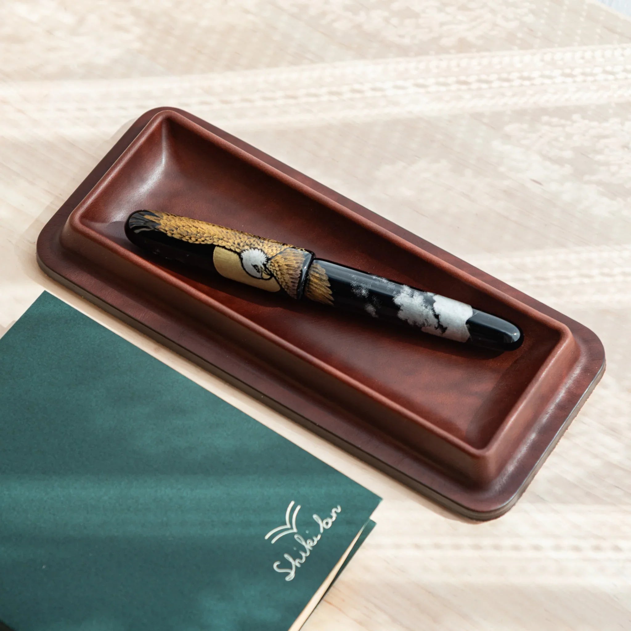 Dark brown Tatsuno leather pen tray displaying a Japanese fountain pen with bird maki-e.