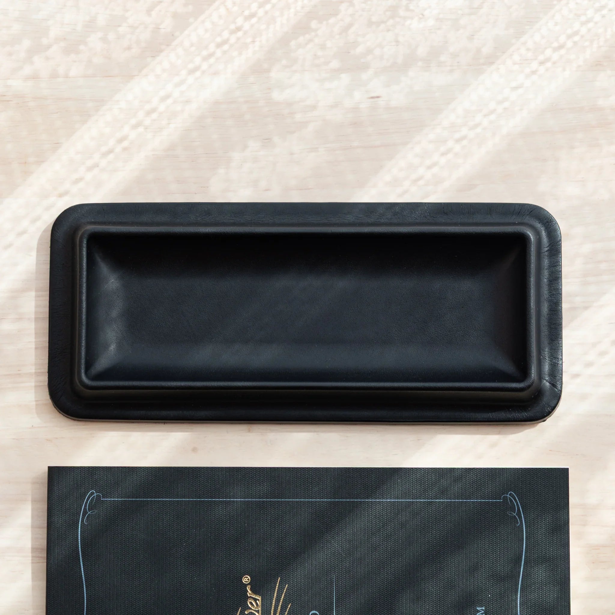 Top-down view of empty black Tatsuno Leather Pen Tray on wooden surface.
