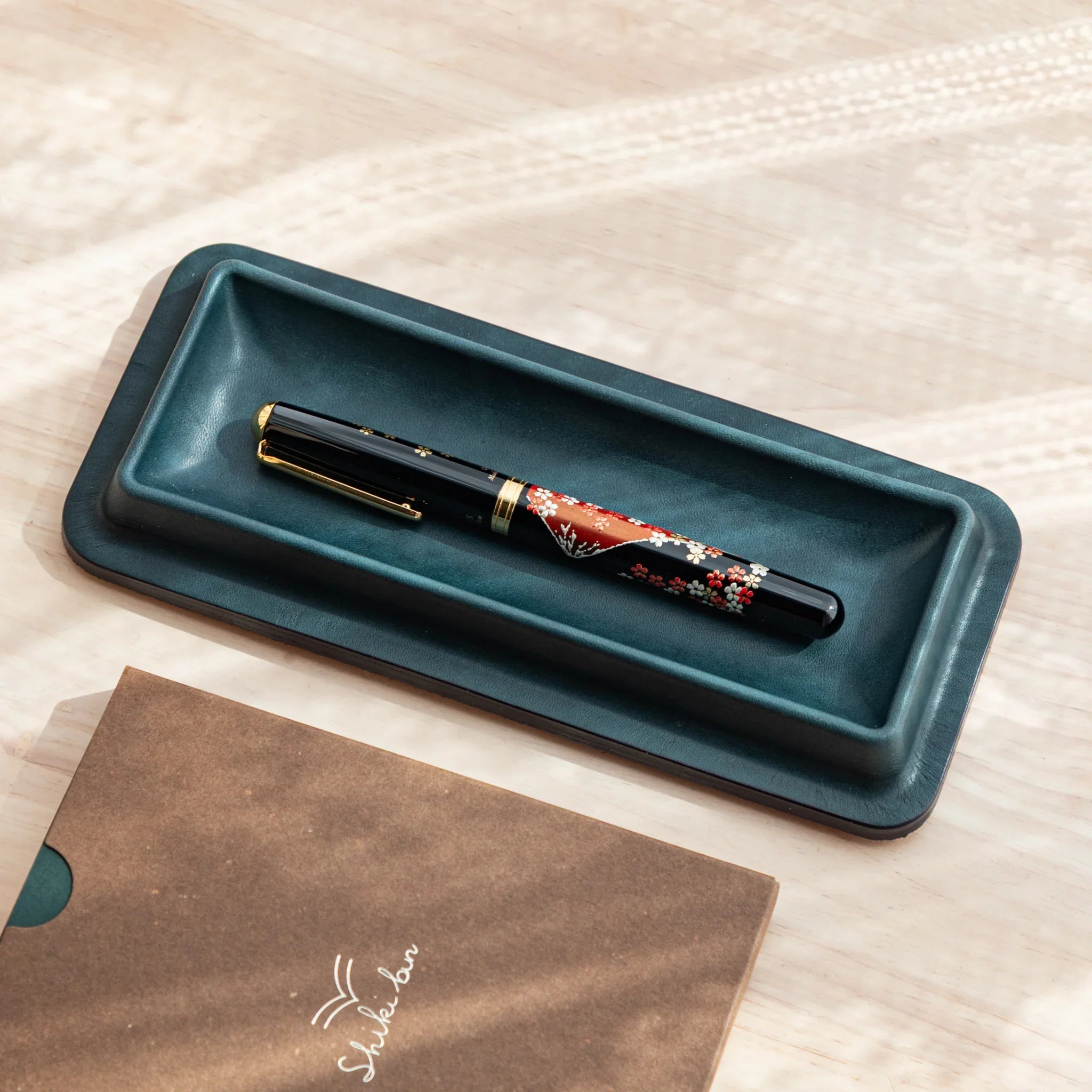 Tatsuno Leather Pen Tray Slim in dark green holding a Japanese Fountain Pen, placed beside Shikibon notebook.