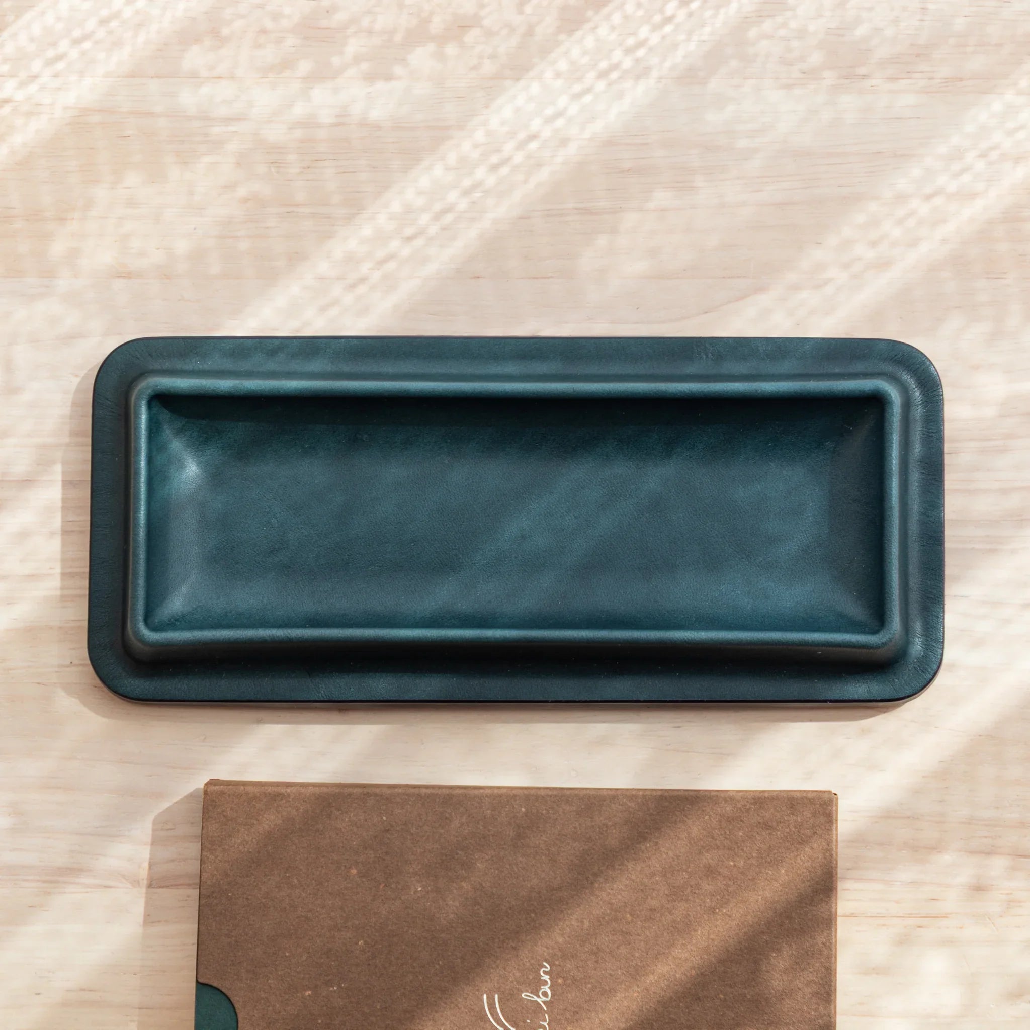 Empty dark green Tatsuno Leather Pen Tray Slim shown from top view with brown folder.