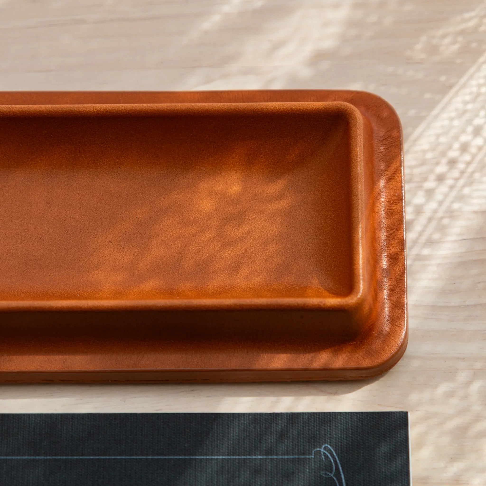 Simple brown Japanese pen tray with smooth leather finish and raised edges.