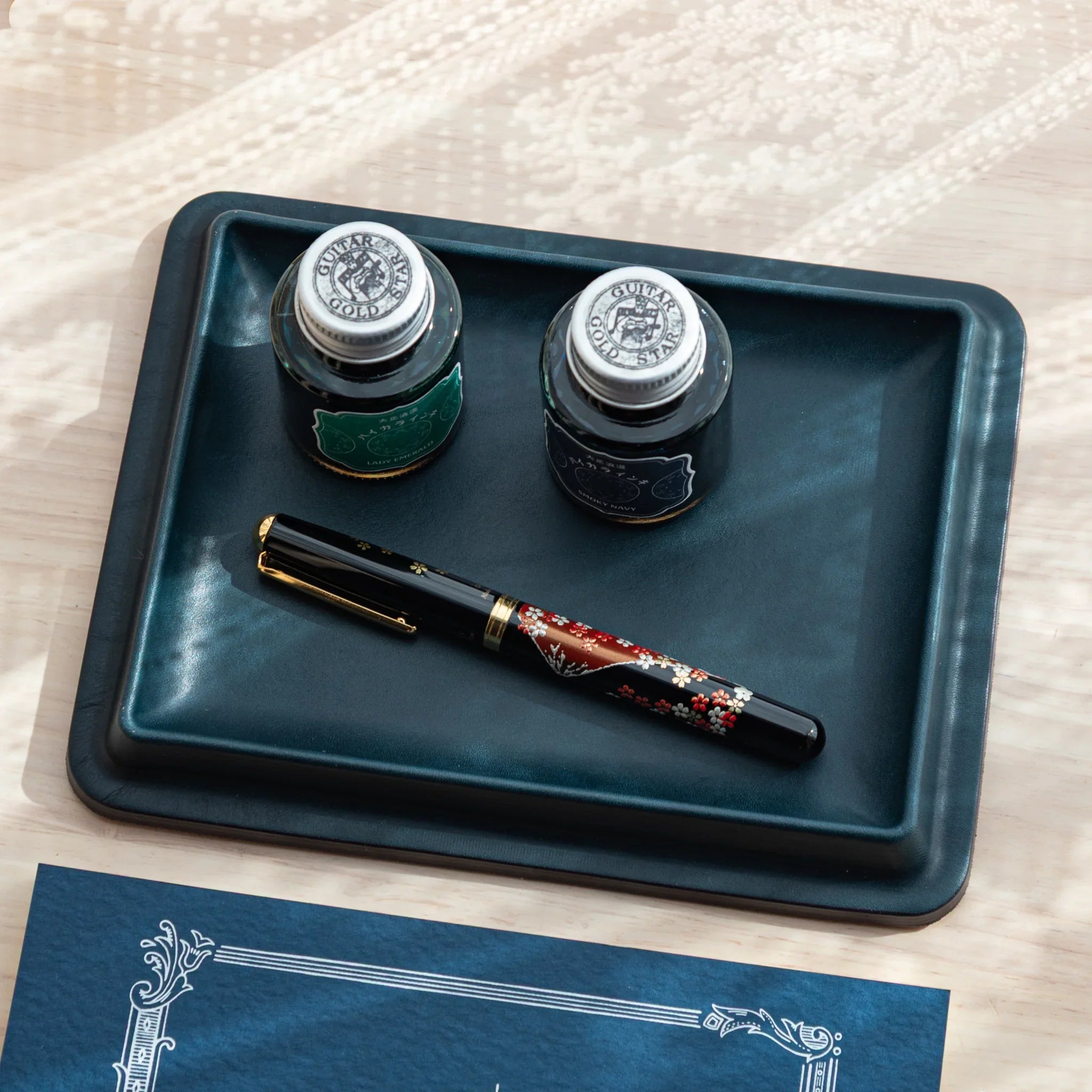 Japanese Pen Tray in deep blue leather, holding two ink bottles and a lacquered fountain pen.